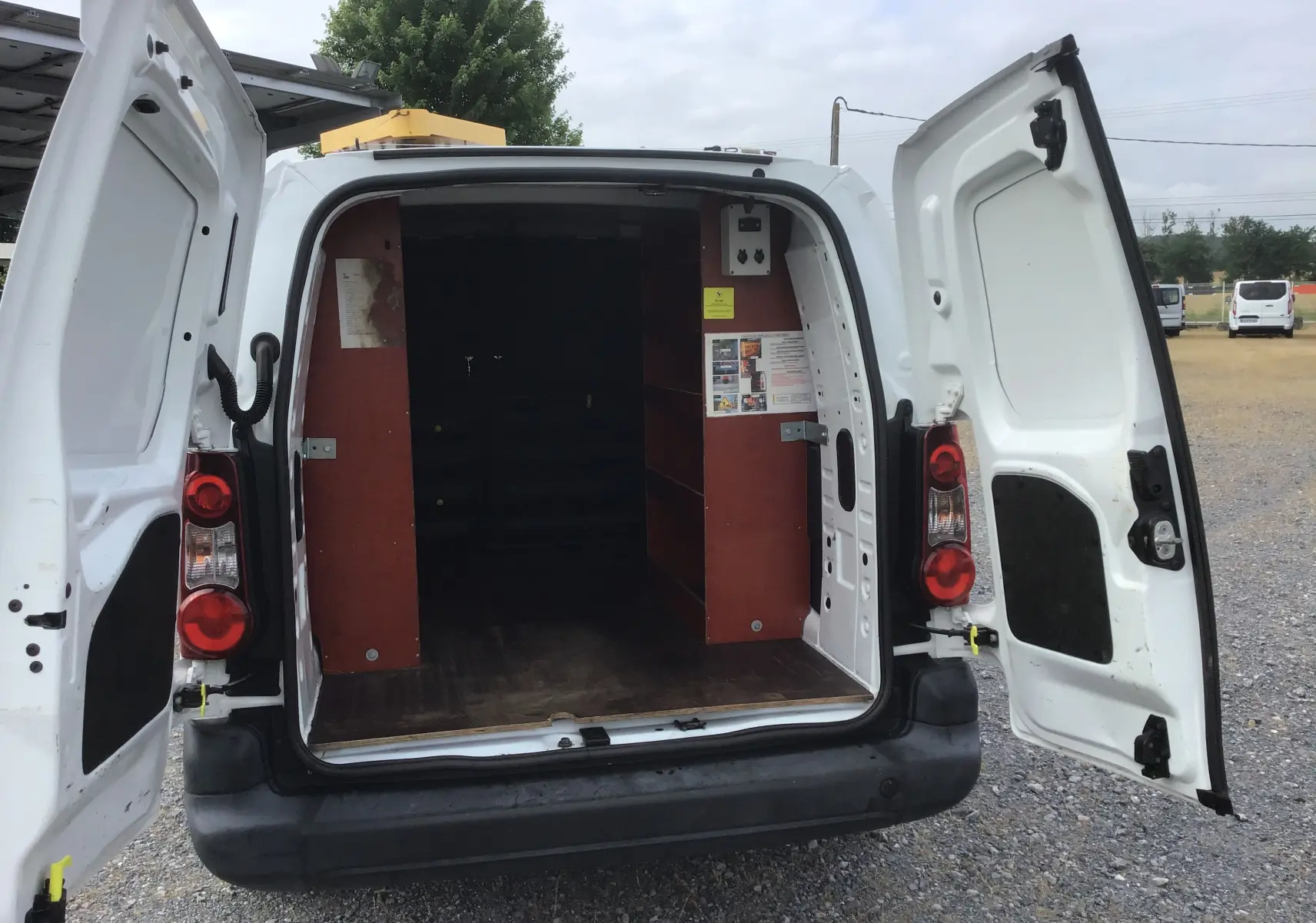 Vue arrière d’un Citroën Berlingo XL blanc 2018 avec portes ouvertes montrant l’intérieur aménagé de rangements en bois.