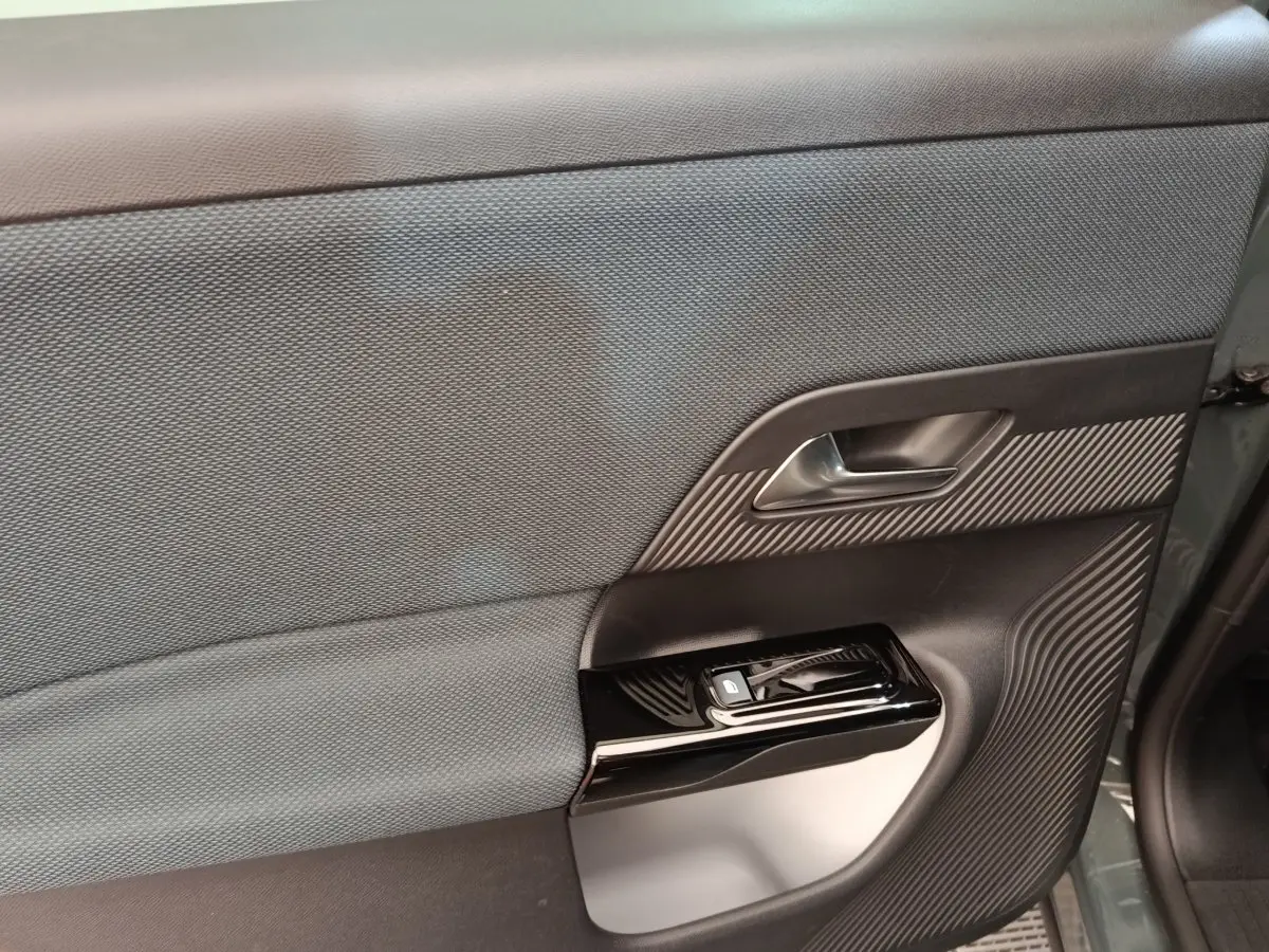 Gros plan sur la porte intérieure côté gauche du Citroën C5 hybride vert 2026 avec garniture textile et commandes de fenêtre.