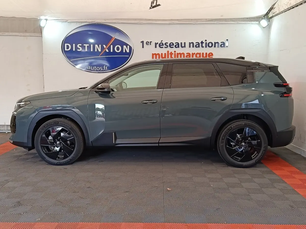 Vue de profil côté gauche d'un Citroën C5 hybride vert avec jantes noires et toit noir dans un showroom.