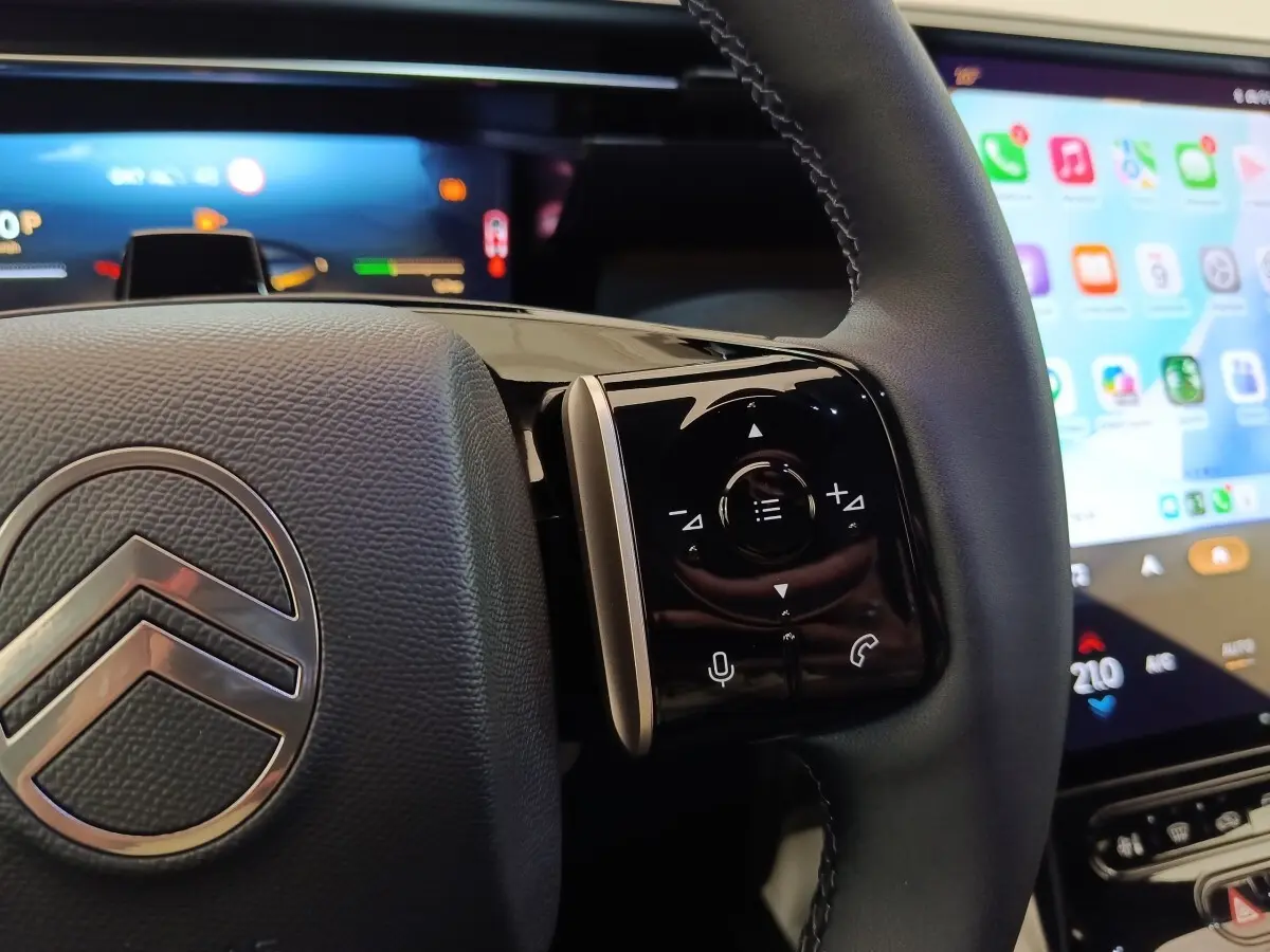Gros plan sur le volant cuir noir de la Citroën C5 hybride, avec commandes multifonctions et écran tactile en arrière-plan.