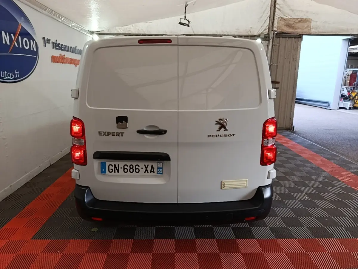 Vue arrière d’un Peugeot Expert Fourgon blanc garé dans un garage avec feux arrière allumés.