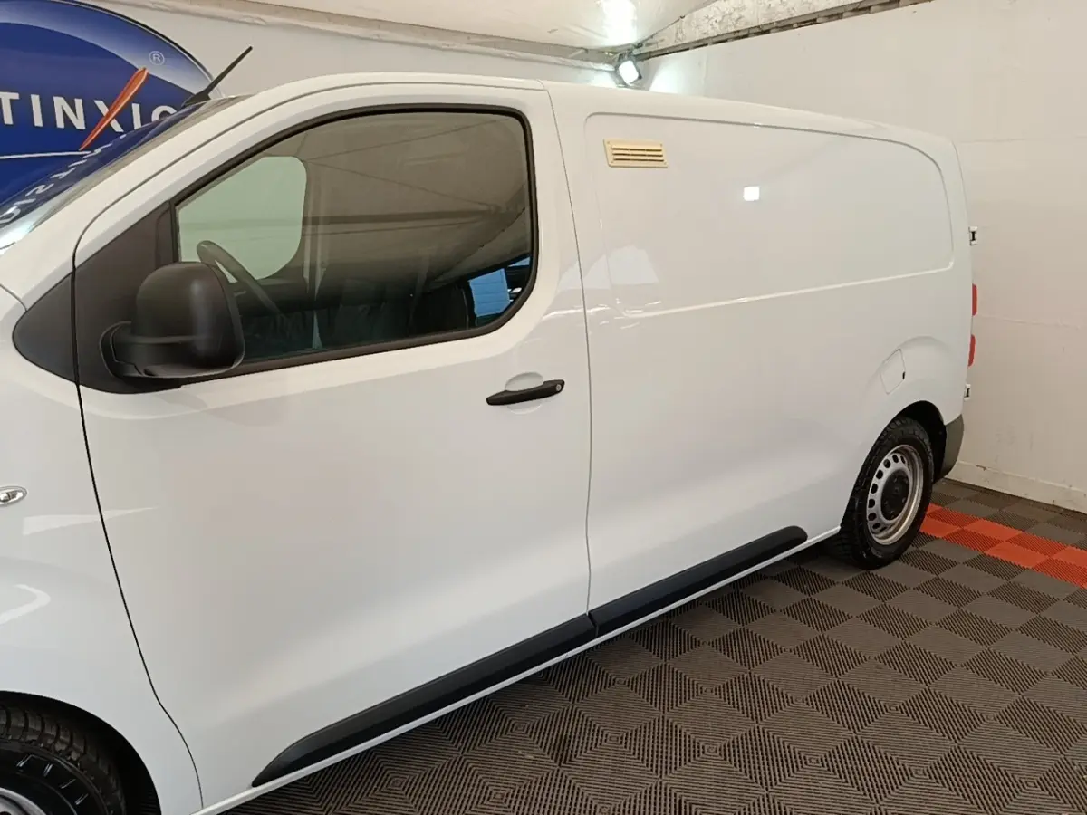 Vue de profil côté gauche d'un Peugeot Expert Fourgon blanc stationné sur un sol à damiers gris et orange.