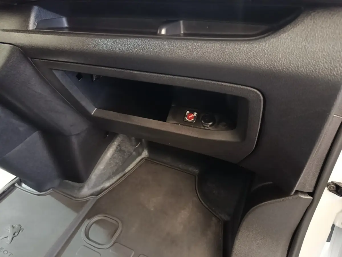 Vue intérieure côté passager du Peugeot Expert Fourgon blanc, avec rangement ouvert et moquette noire au sol.