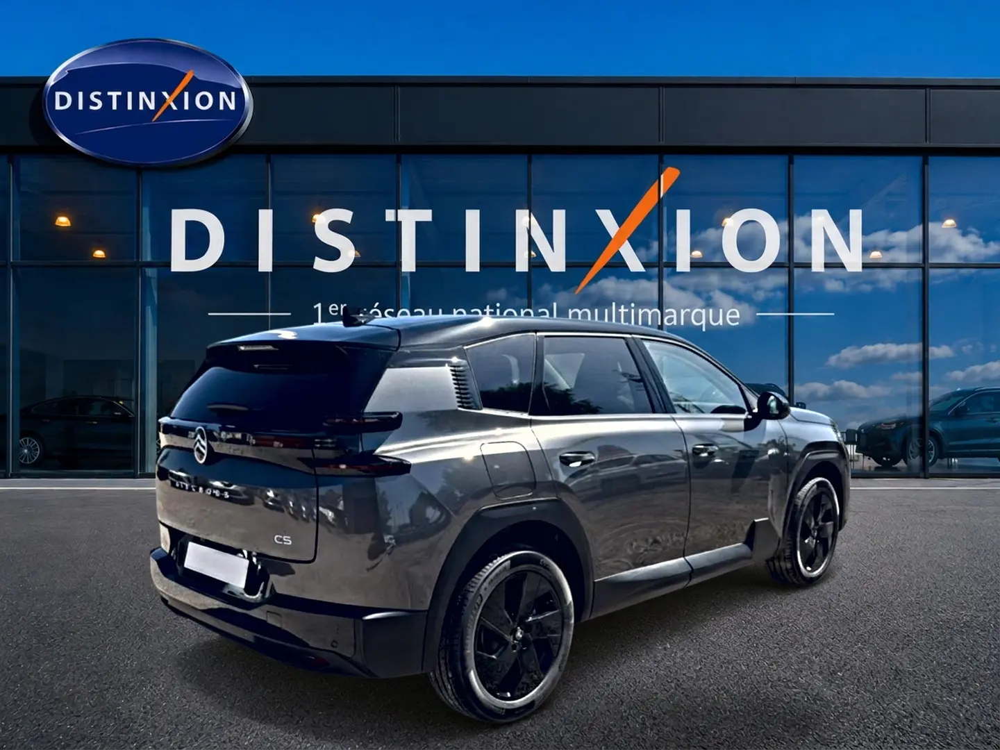 Vue 3/4 arrière droite du Citroën C5 Aircross gris platinium avec toit noir et jantes alliage noires devant un showroom.