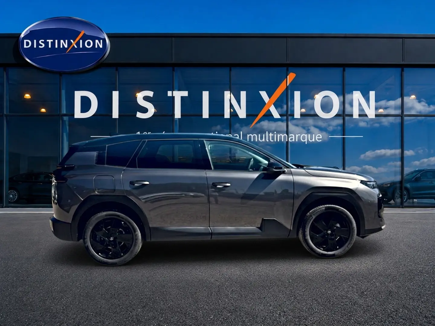 Profil droit du Citroën C5 Aircross gris platinium avec toit noir et jantes alliage noires devant une vitrine Distinxion.