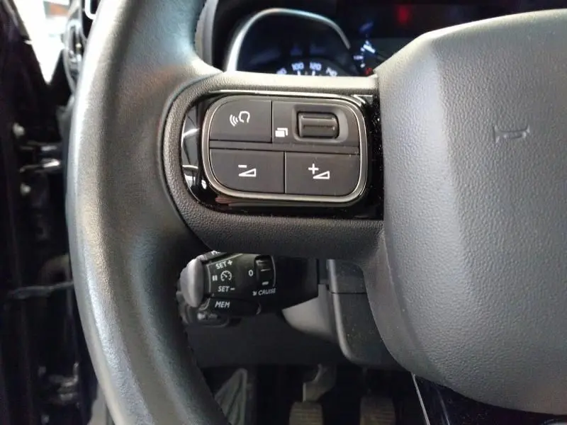 Gros plan sur les commandes au volant du Citroën C3 Aircross noir perla nera, mettant en valeur les boutons de réglage audio et régulateur.