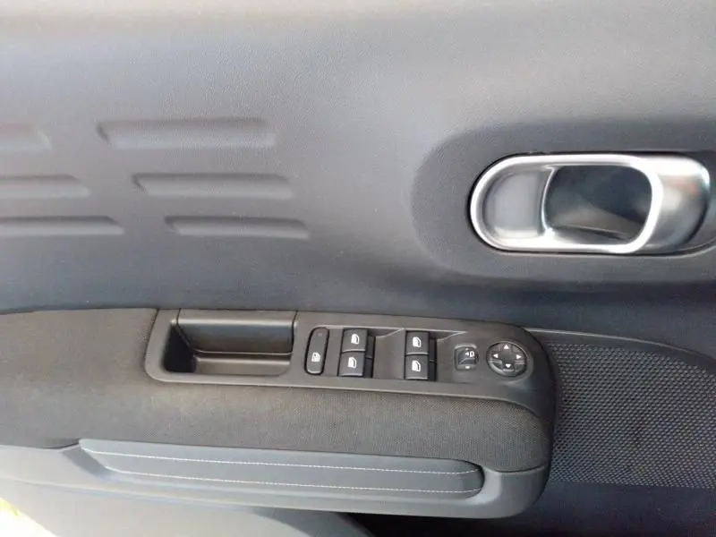 Détail de la porte côté conducteur du Citroën C3 Aircross noir perla nera, avec commandes des vitres et poignée intérieure chromée.