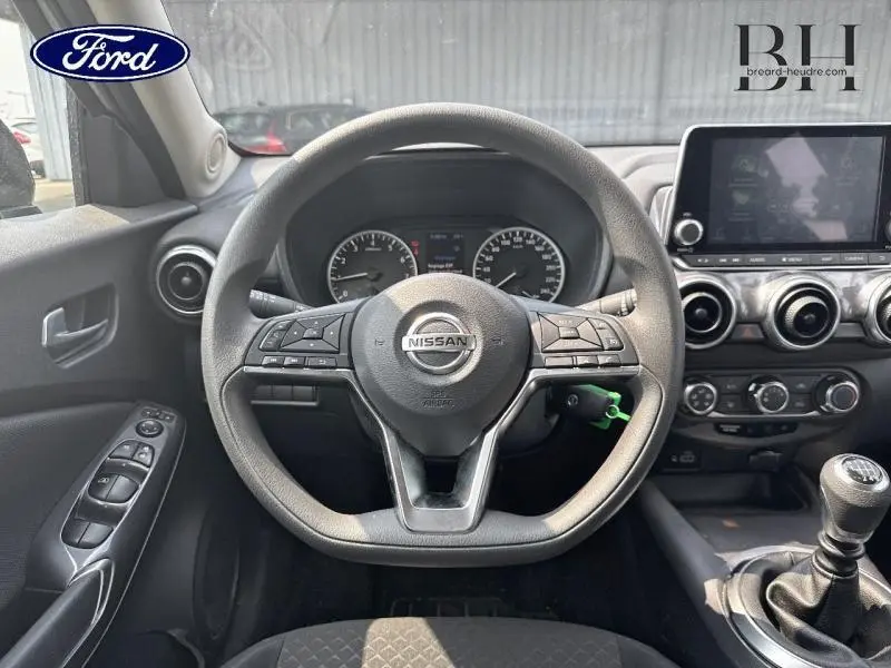 Vue intérieure centrée sur le volant Nissan du Juke gris perle, avec tableau de bord et commande de boîte manuelle visibles.