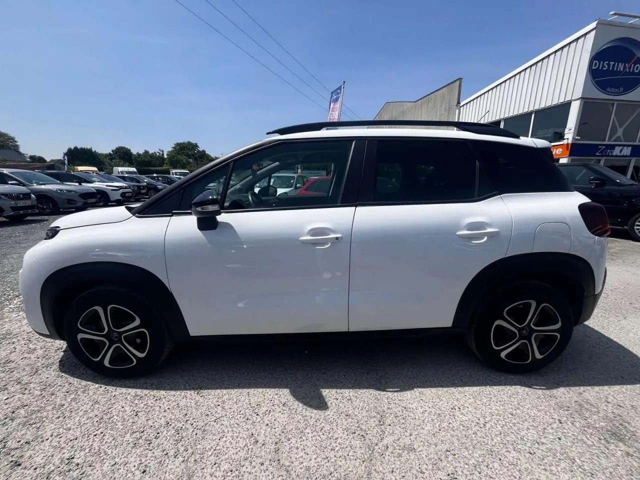 Profil côté gauche d'un Citroën C3 Aircross blanc banquise 2023 avec toit blanc opale et barres de toit noires brillantes.