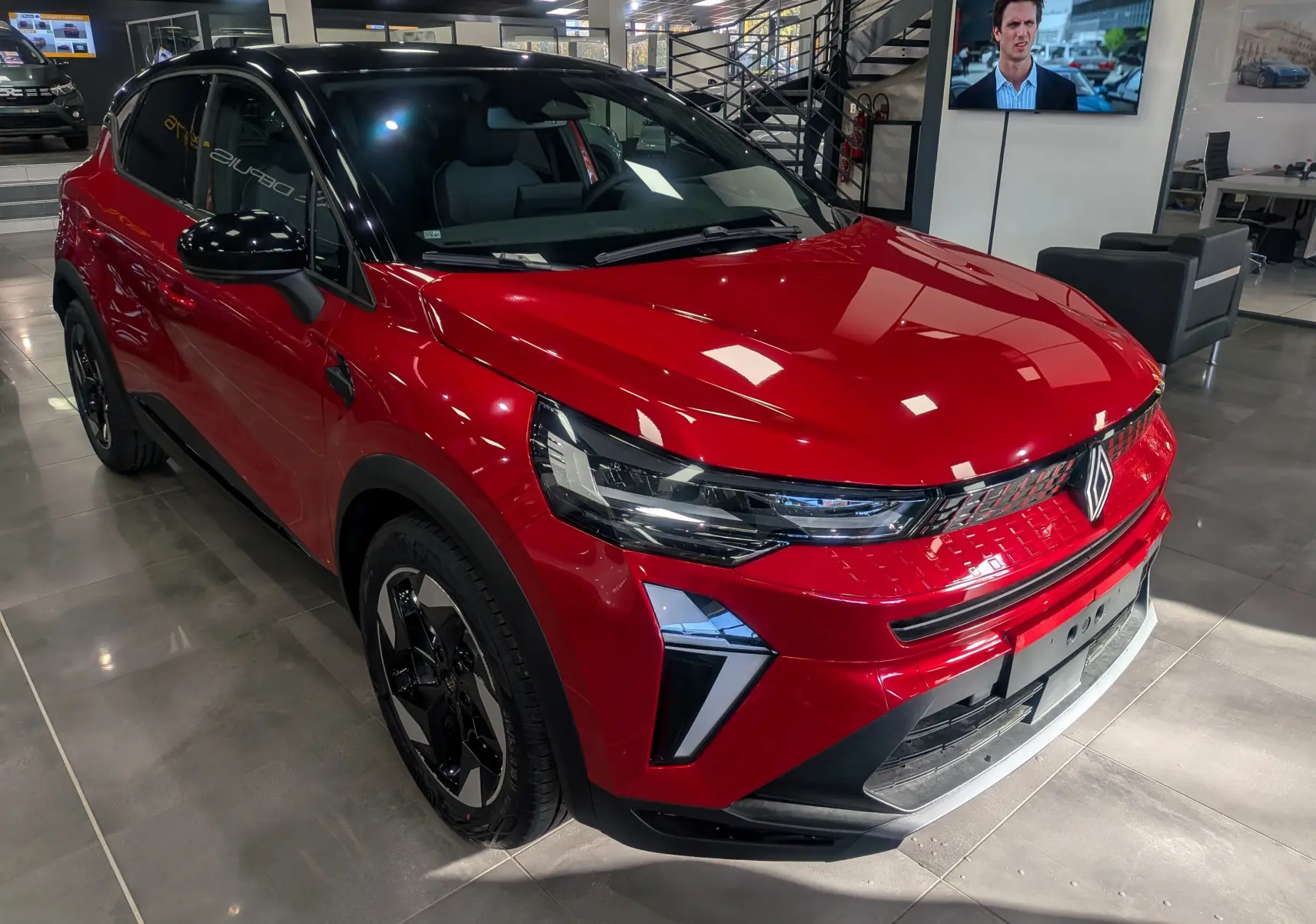 Vue 3/4 avant droite du Renault Captur E-TECH rouge Flamme avec toit noir et jantes noires en showroom.