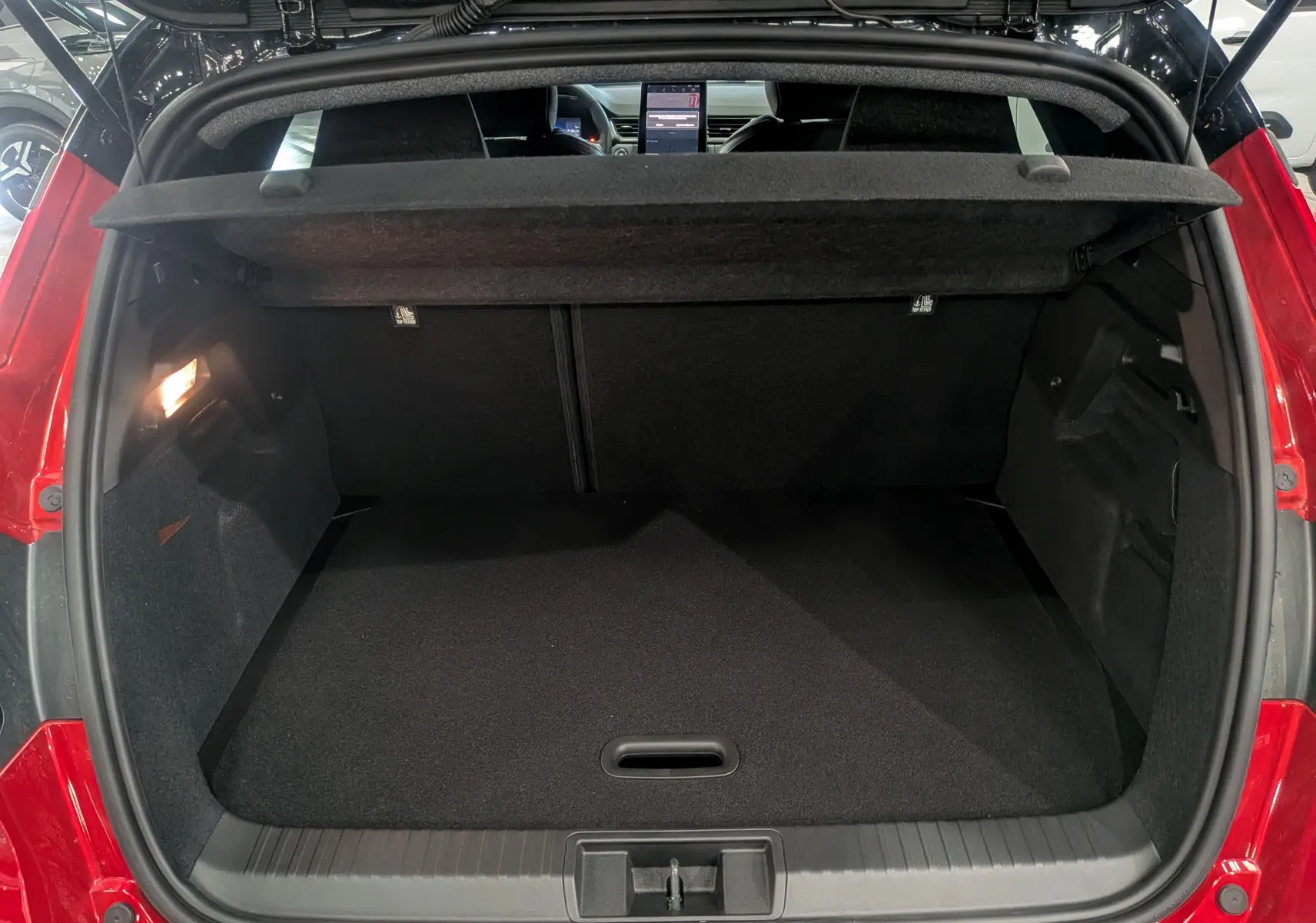 Coffre ouvert vu de l'arrière d'un Renault Captur E-Tech rouge flamme avec toit noir, intérieur sombre et tablette arrière relevée.