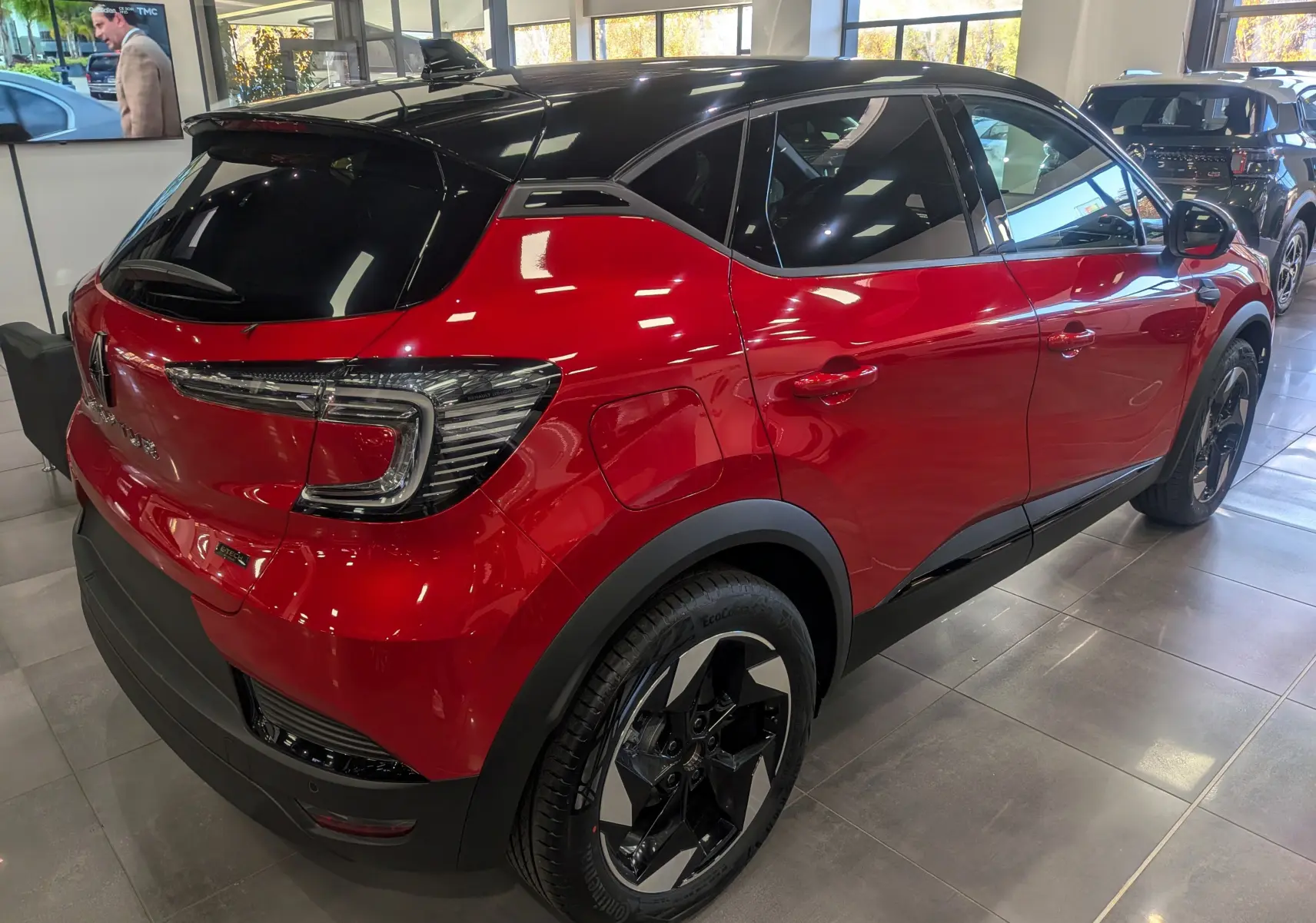 Vue 3/4 arrière droite du Renault Captur E-TECH rouge Flamme avec toit noir brillant en showroom.