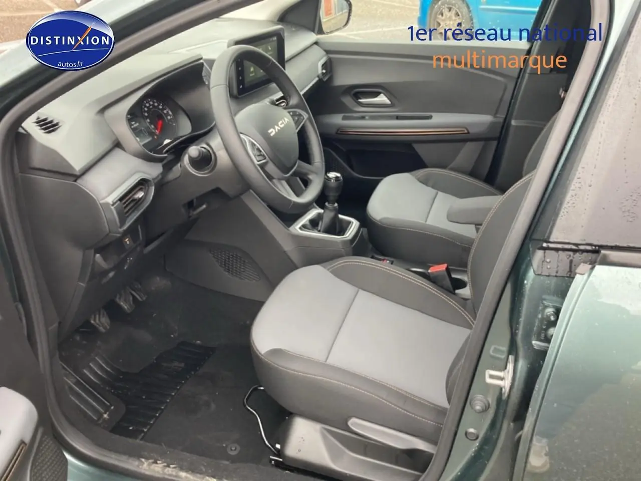 Intérieur avant droit du Dacia Jogger vert cèdre 2025, avec volant, sièges gris et boîte manuelle visible.