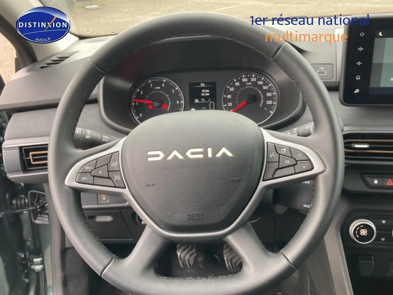 Vue intérieure centrée sur le volant DACIA du Jogger 2025 avec commandes intégrées et tableau de bord visible.