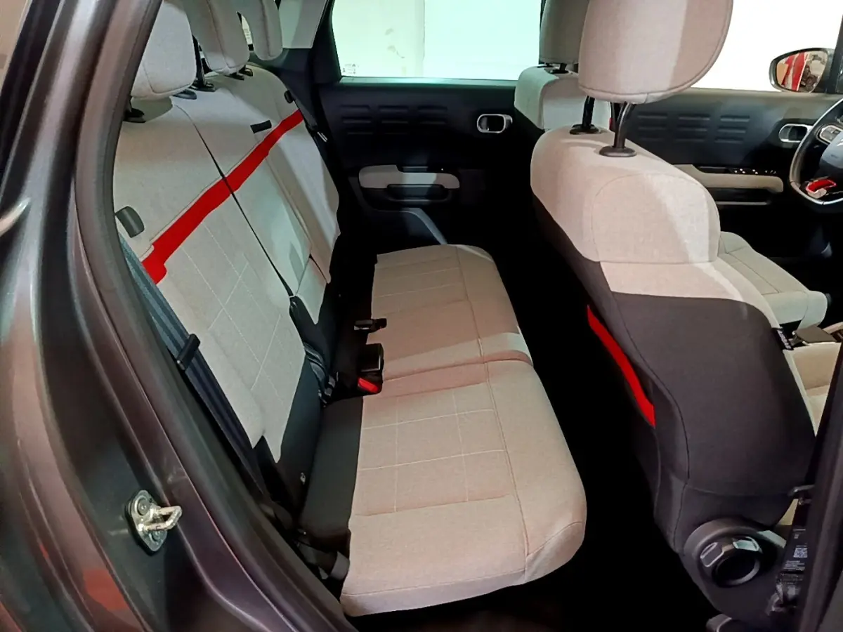 Vue intérieure côté gauche montrant la banquette arrière beige avec bande rouge du Citroën C3 Aircross gris foncé.