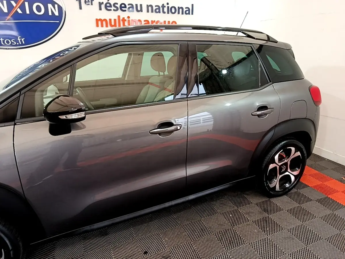 Vue de profil côté gauche d'un Citroën C3 Aircross gris foncé avec toit noir et jantes distinctives.