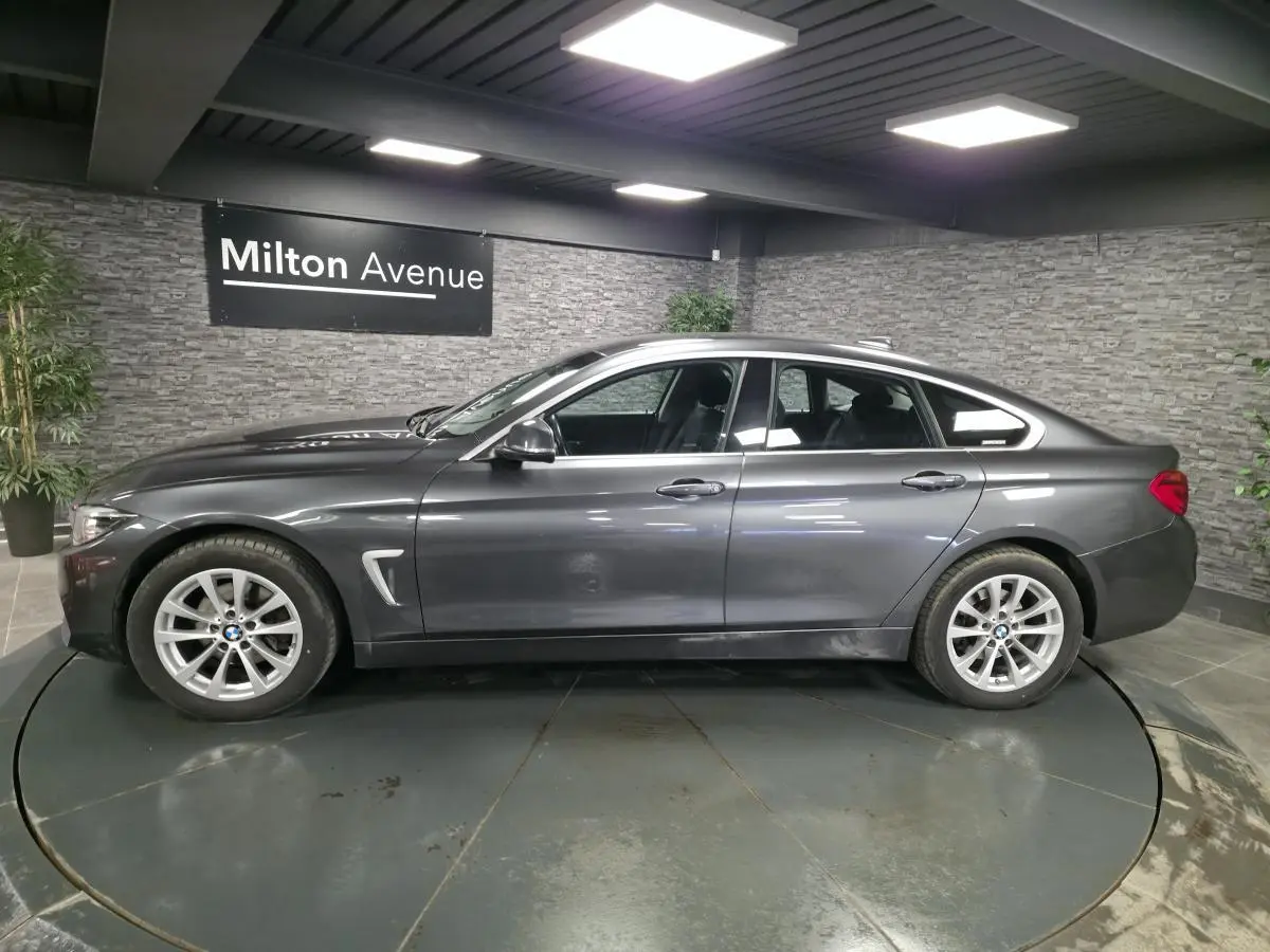 BMW Série 4 Gran Coupé gris foncé vue de profil côté gauche avec jantes alliage 17 pouces en intérieur showroom.