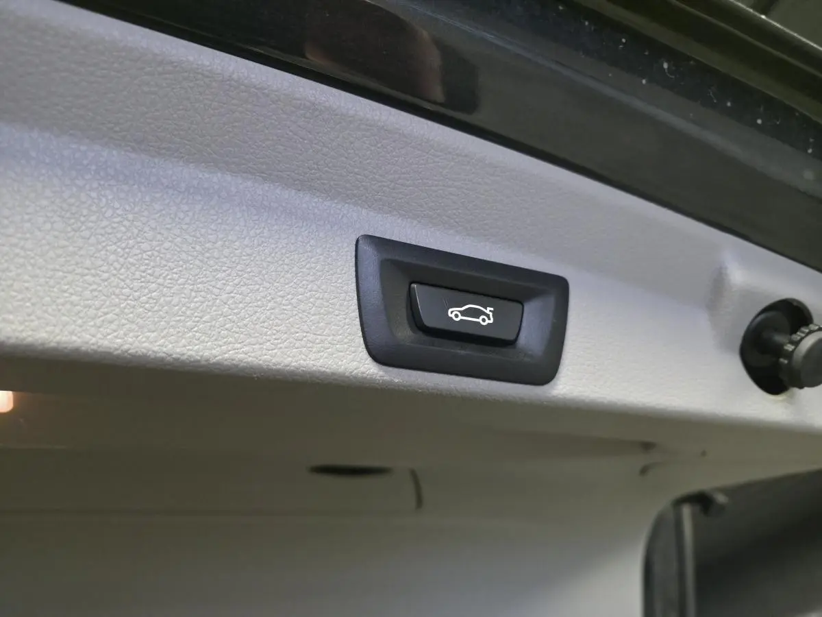 Bouton d'ouverture électrique du hayon sur la face intérieure du coffre d'une BMW Série 4 gris foncé.