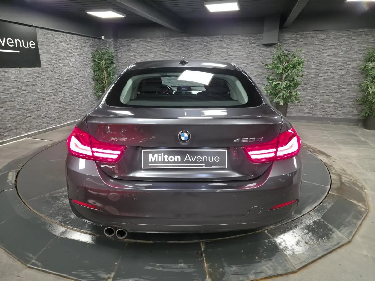 Vue arrière d'une BMW Série 4 420d xDrive Gran Coupé gris foncé avec feux LED allumés en intérieur showroom.