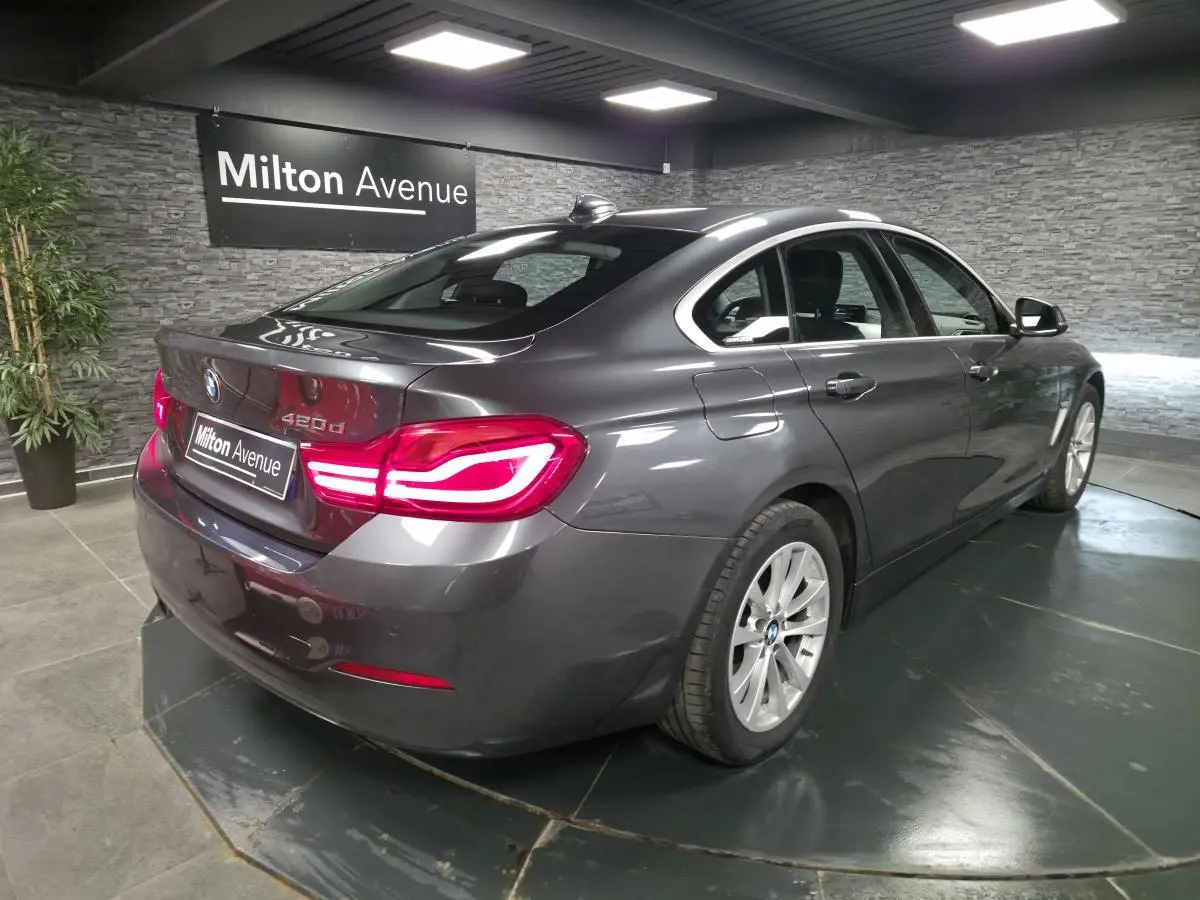BMW Série 4 420d xDrive Gran Coupé gris foncé vue 3/4 arrière droit avec feux arrière LED allumés.