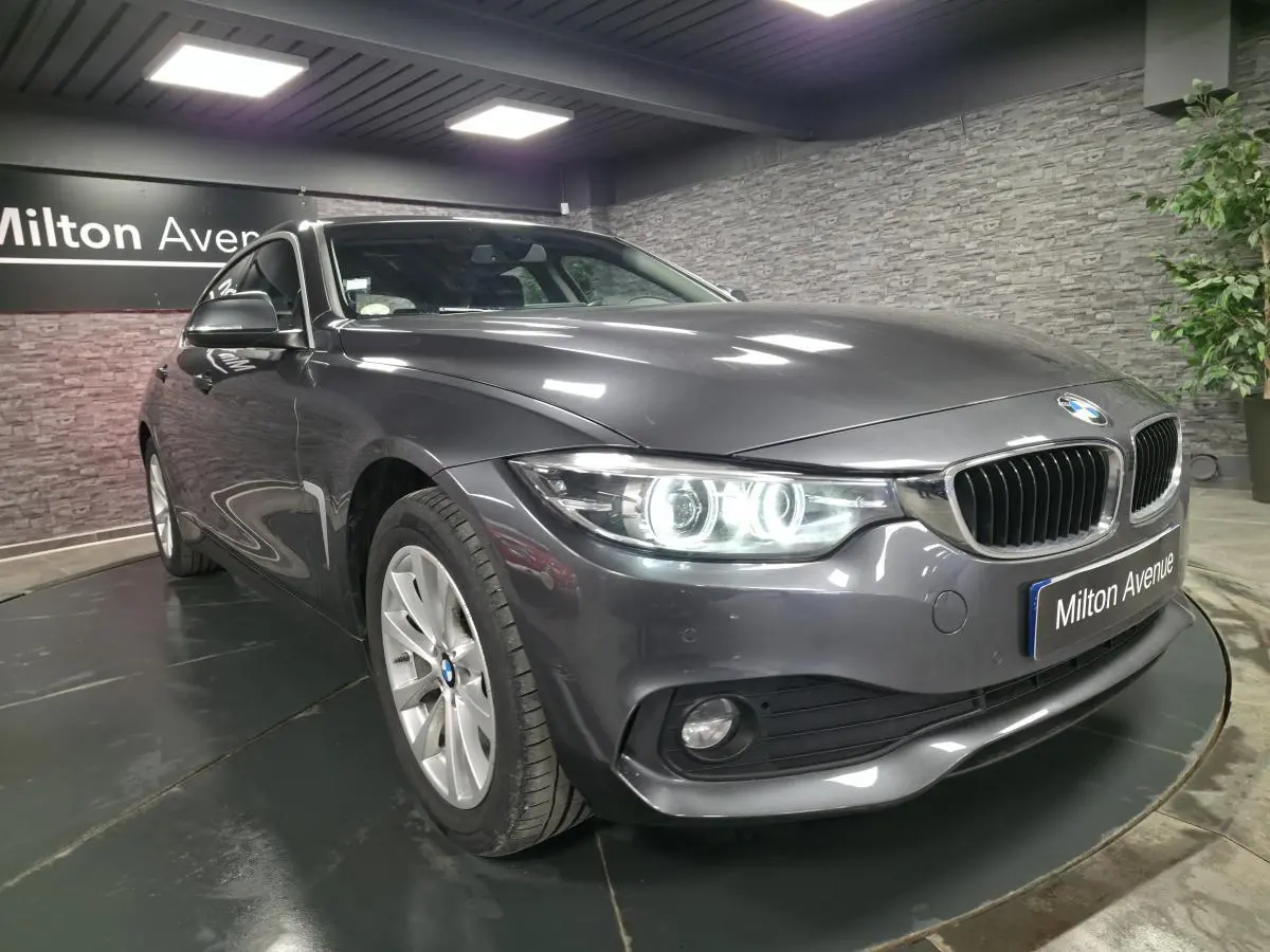 BMW Série 4 Gran Coupé gris foncé vue 3/4 avant avec phares LED allumés et calandre chromée.