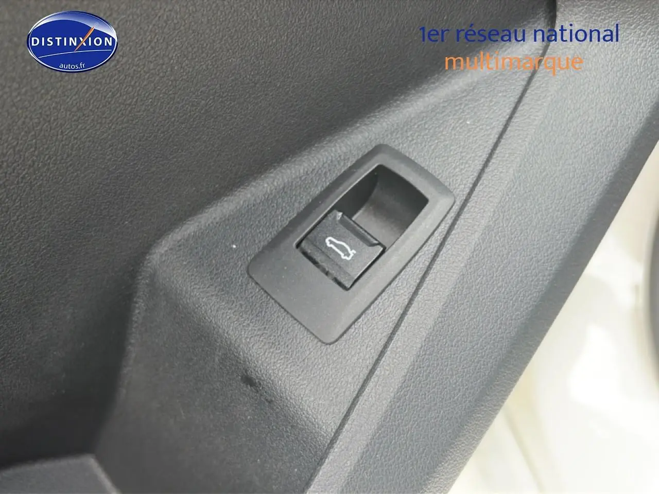 Détail du bouton d'ouverture de coffre sur la porte intérieure d'une BMW Série 1 blanche pure.