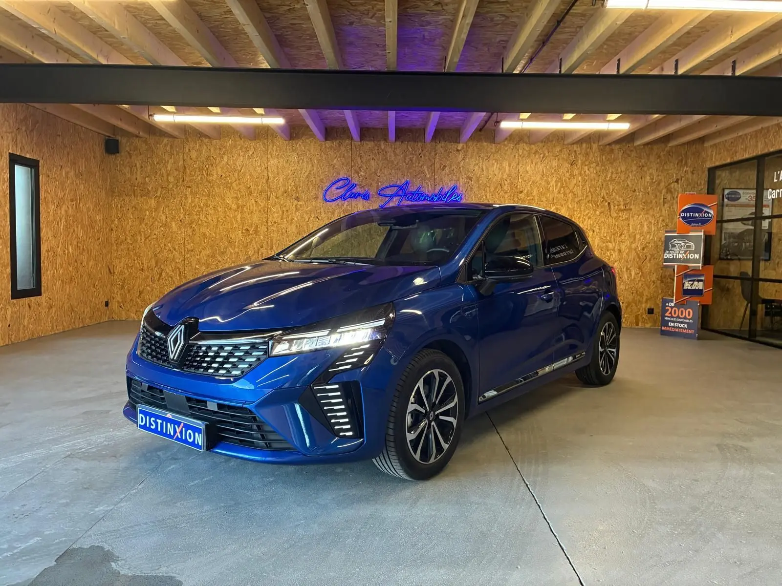 Renault Clio V E-TECH 145 TECHNO bleu iron vue 3/4 avant en intérieur avec éclairage LED et jantes bi-ton.