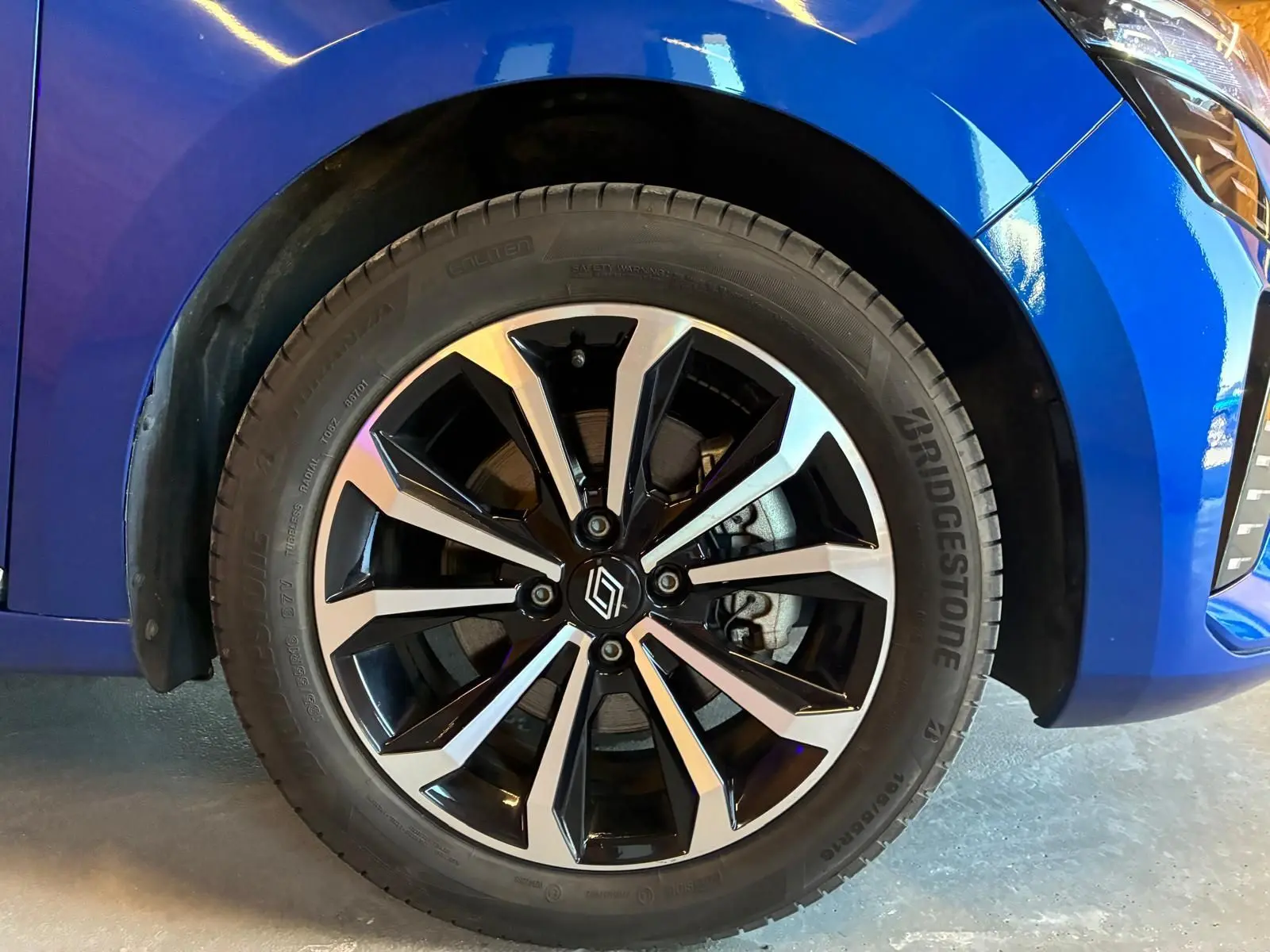 Gros plan sur la roue avant gauche de la Renault Clio V E-TECH 145 TECHNO bleu iron avec jante alliage bicolore et pneus Bridgestone.
