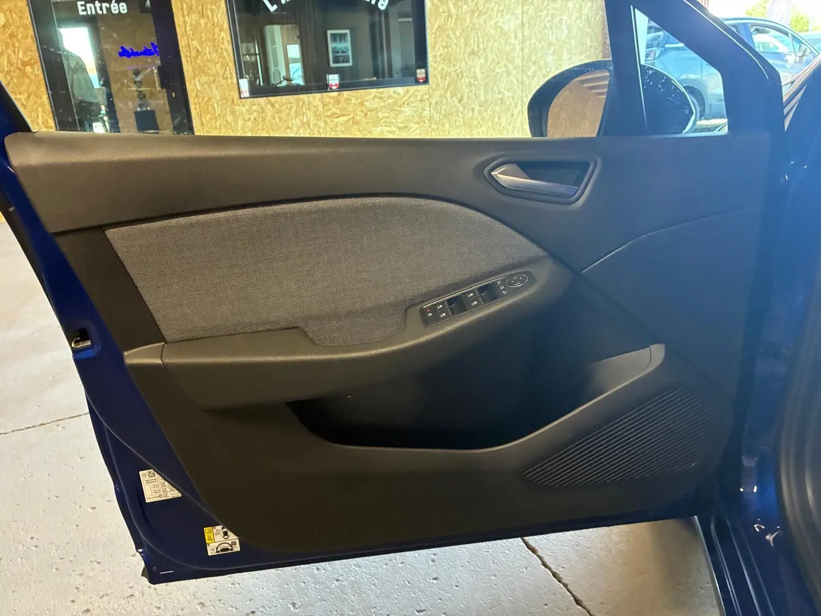 Vue intérieure de la porte avant gauche d'une Renault Clio Bleu Iron 2025, avec commandes de vitres et tissu gris.