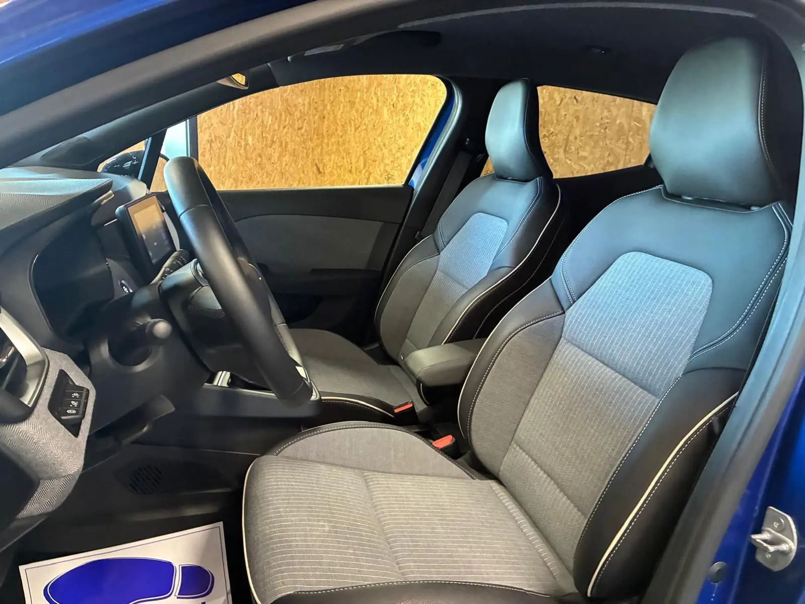 Vue intérieure côté conducteur de la Renault Clio V E-TECH 145 TECHNO 2025, sièges tissu gris noir et volant visible.