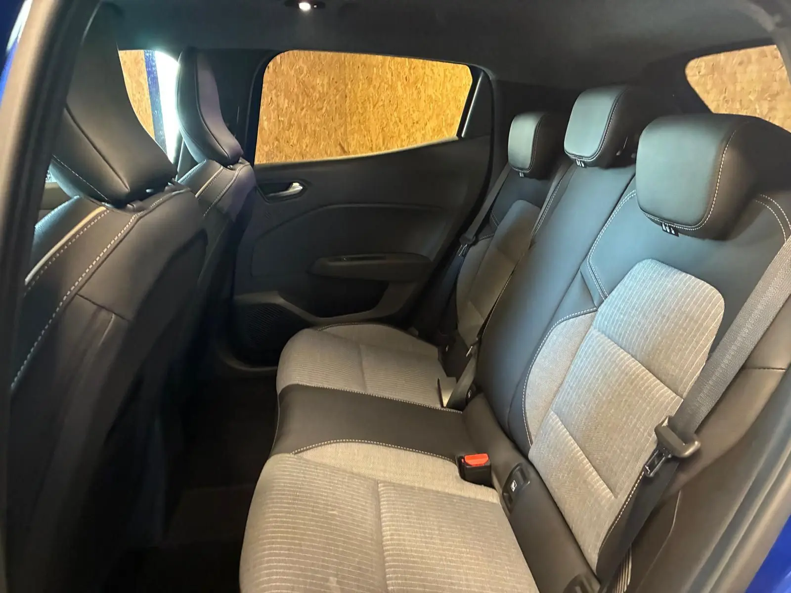Vue intérieure arrière côté gauche de la Renault Clio V E-TECH 145 TECHNO 2025, sièges tissu gris et noir, portières bleu iron.