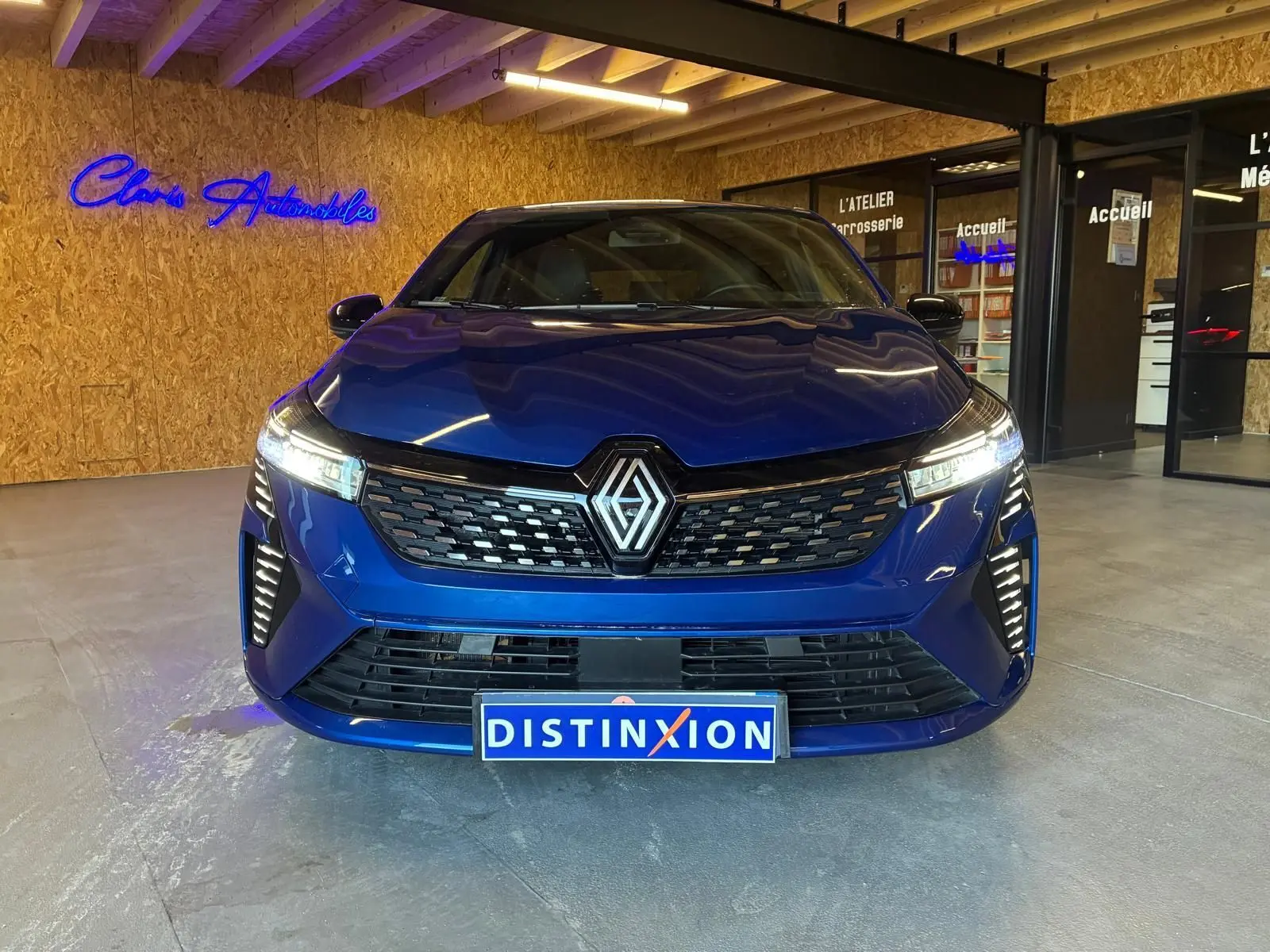 Vue de face d'une Renault Clio V E-TECH 145 TECHNO bleu iron avec calandre noire et phares LED allumés.