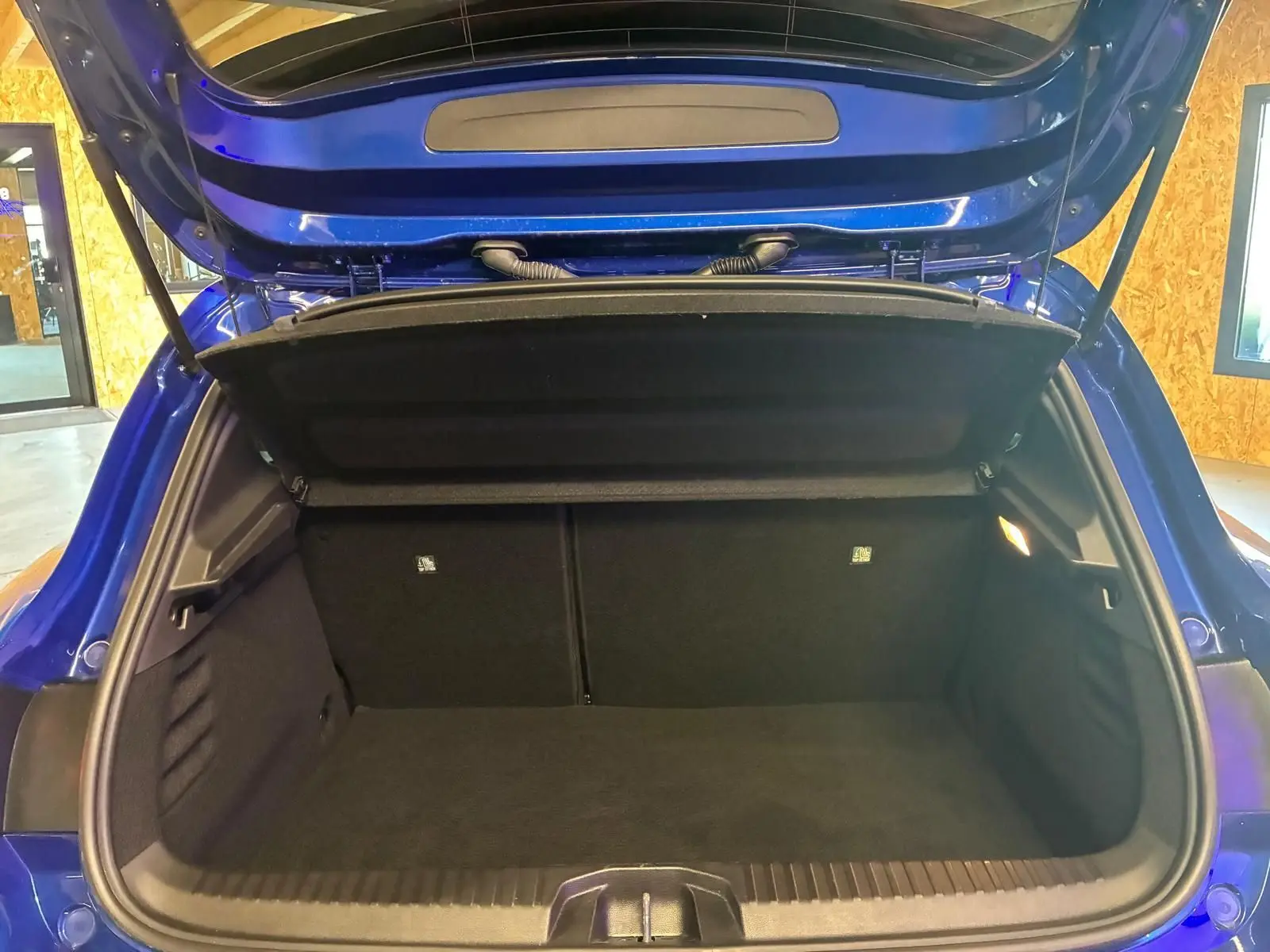 Coffre ouvert vu de l'arrière d'une Renault Clio V E-TECH 145 TECHNO bleu Iron, intérieur noir et espace de chargement vide.