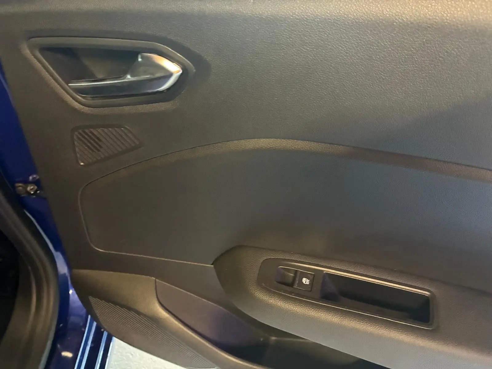 Vue rapprochée de la porte intérieure côté gauche d'une Renault Clio 2025 bleu Iron, avec poignée et commande de vitre.