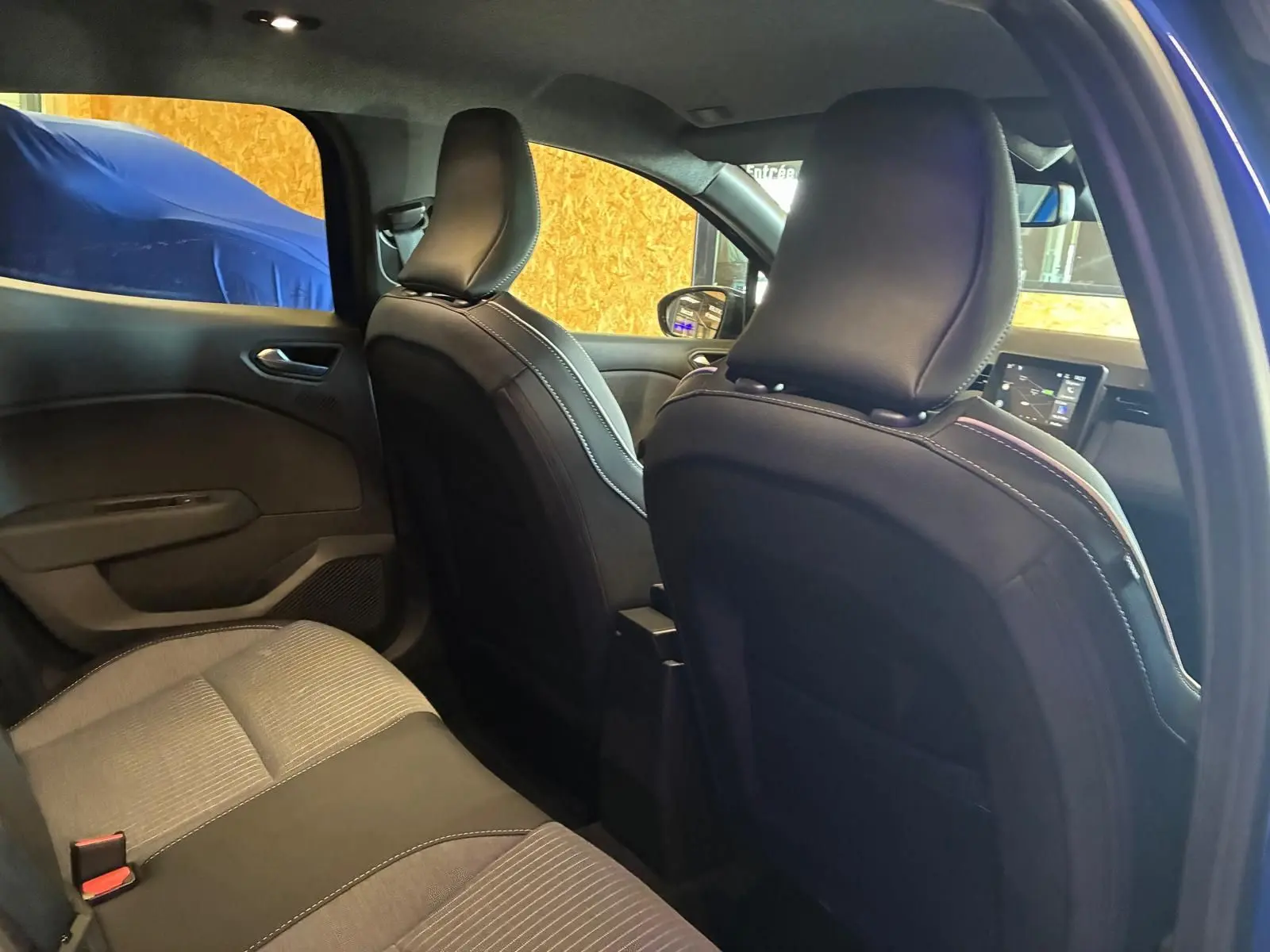 Vue intérieure arrière de la Renault Clio V E-Tech 145 en bleu Iron, sièges tissu gris noir et tableau de bord visible.
