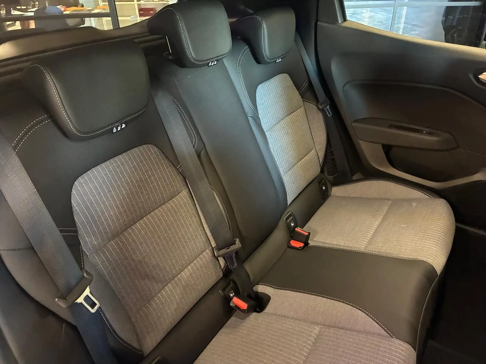Vue intérieure arrière de la Renault Clio V E-TECH 145 TECHNO 2025, sièges tissu gris et noir avec surpiqûres blanches.