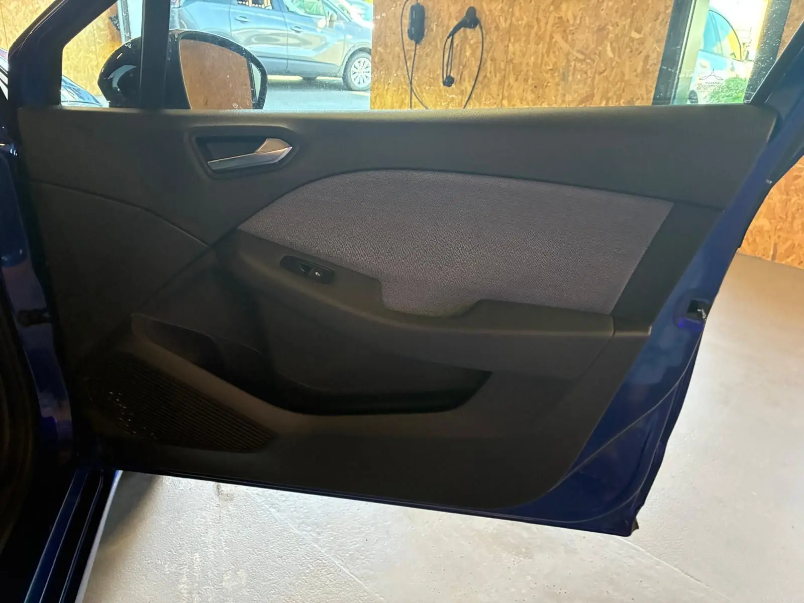 Vue intérieure de la porte avant gauche bleu iron de la Renault Clio V E-TECH 145 TECHNO avec habillage tissu gris et commandes.