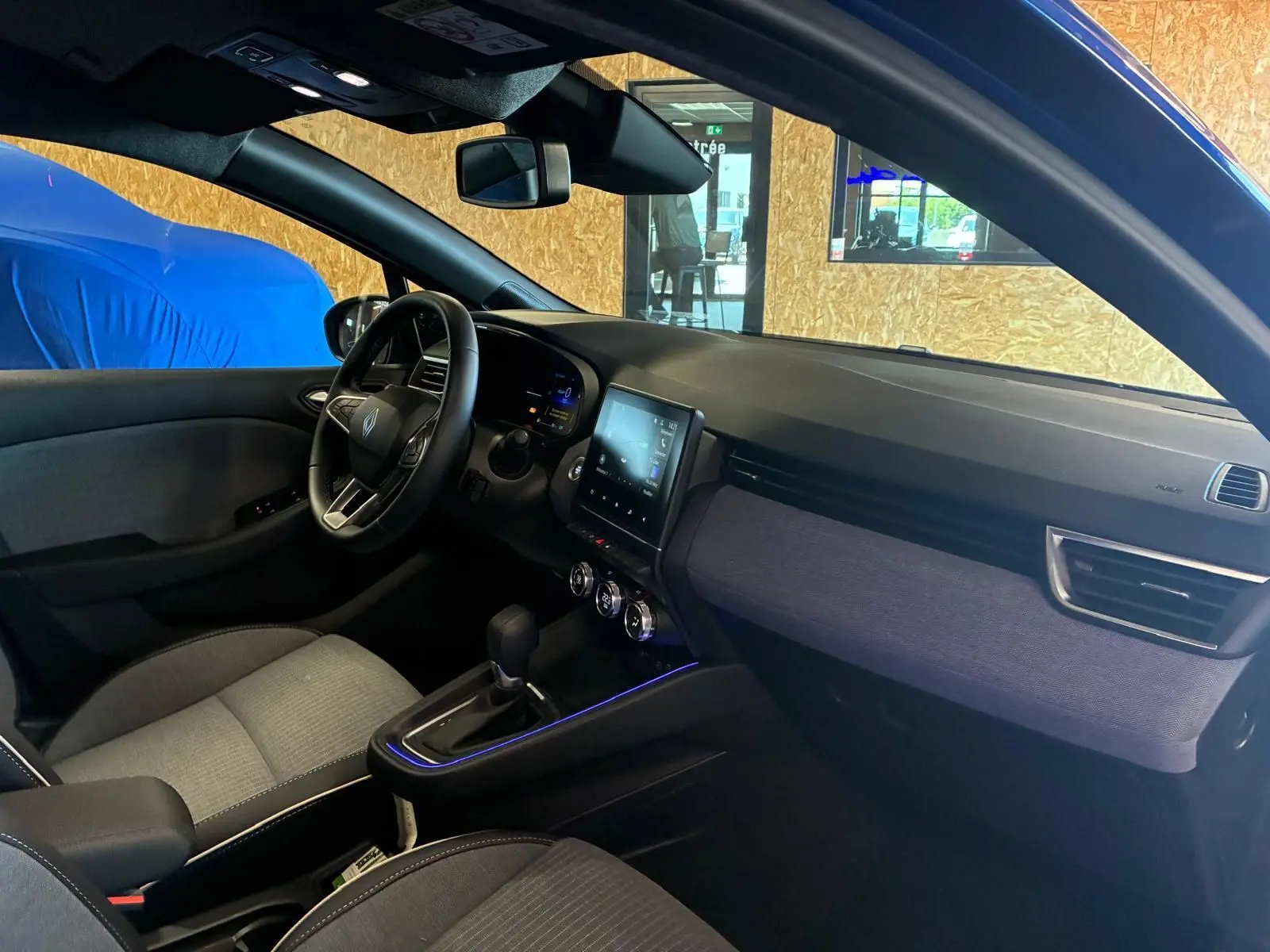 Intérieur avant droit de la Renault Clio V E-TECH 145 TECHNO 2025 avec tableau de bord noir et tissu gris.