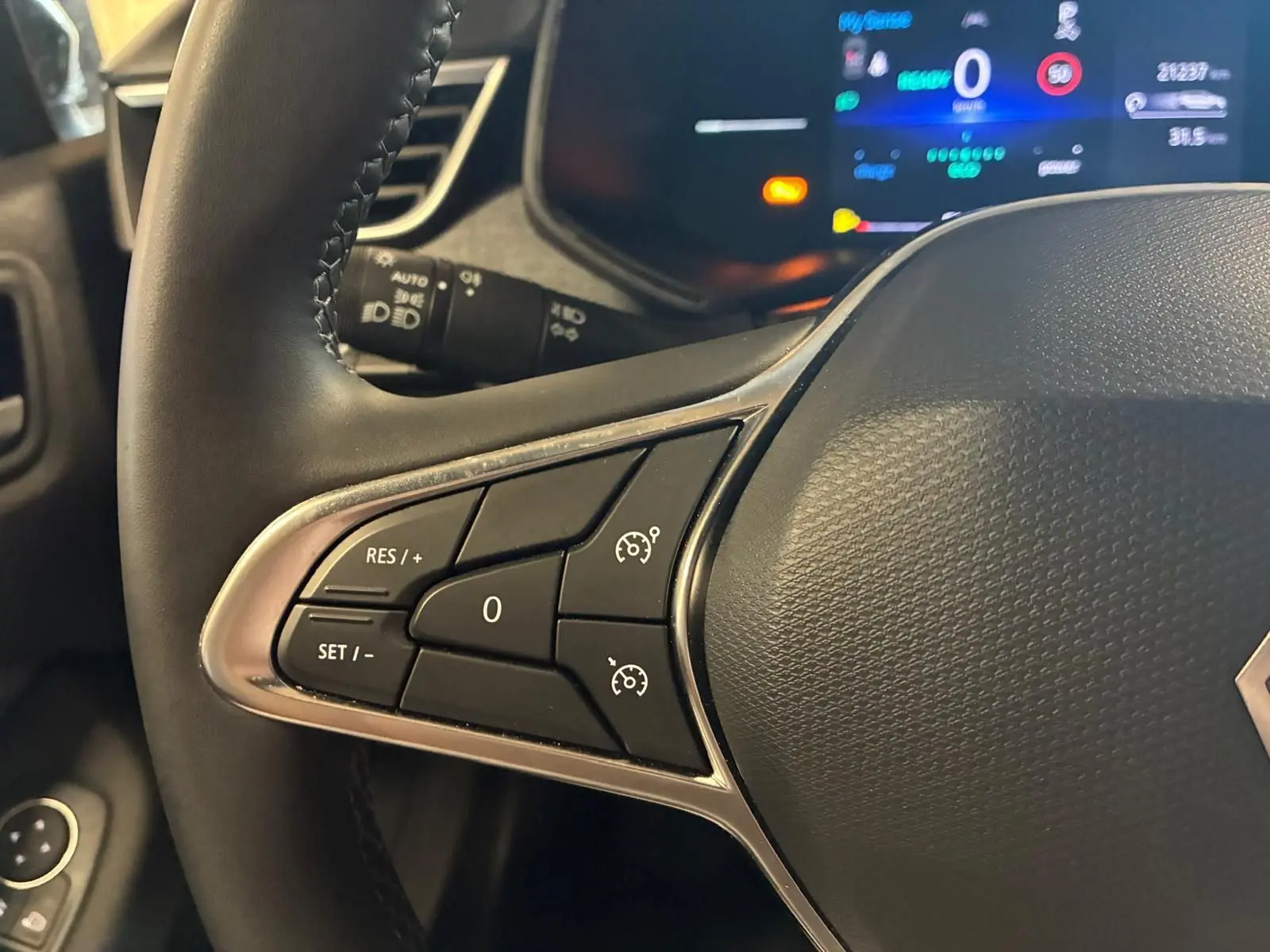 Gros plan sur le volant noir de la Renault Clio V E-TECH 145 TECHNO avec commandes de régulateur de vitesse et tableau de bord numérique.