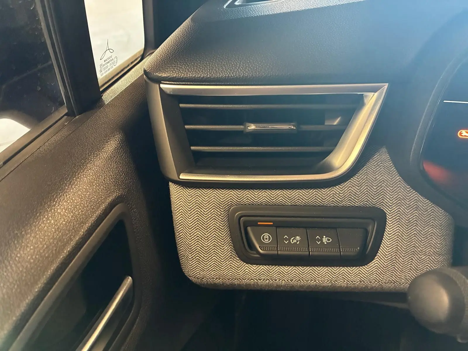 Détail intérieur côté gauche montrant la grille d'aération et les commandes d'éclairage sur tissu gris noir de la Renault Clio 2025.