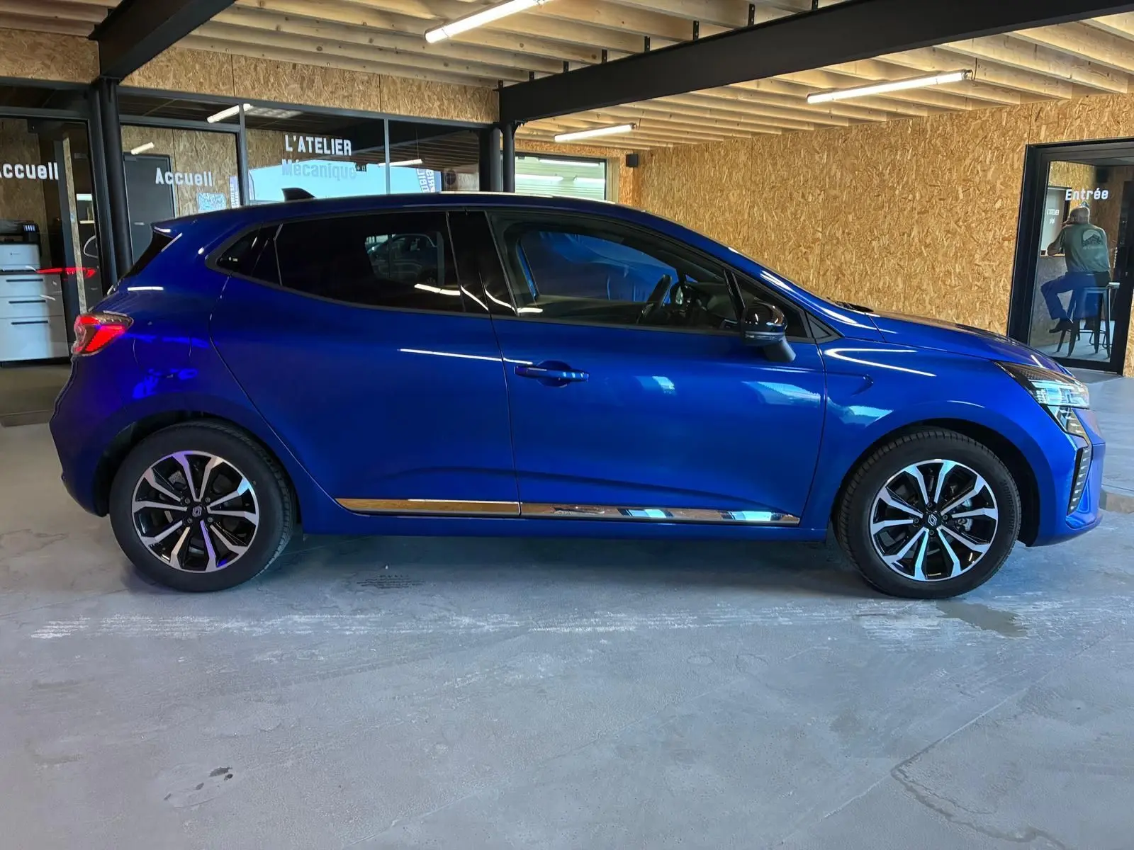 Profil droit d'une Renault Clio V E-TECH 145 TECHNO bleu iron 2025 avec jantes alliage bicolores et vitres teintées.