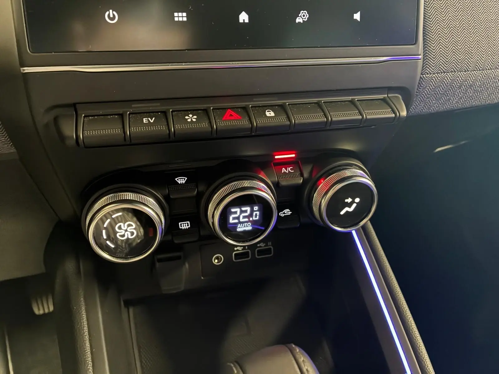 Gros plan sur la console centrale de la Renault Clio V E-TECH 145 TECHNO, avec commandes de climatisation et éclairage d'ambiance bleu.