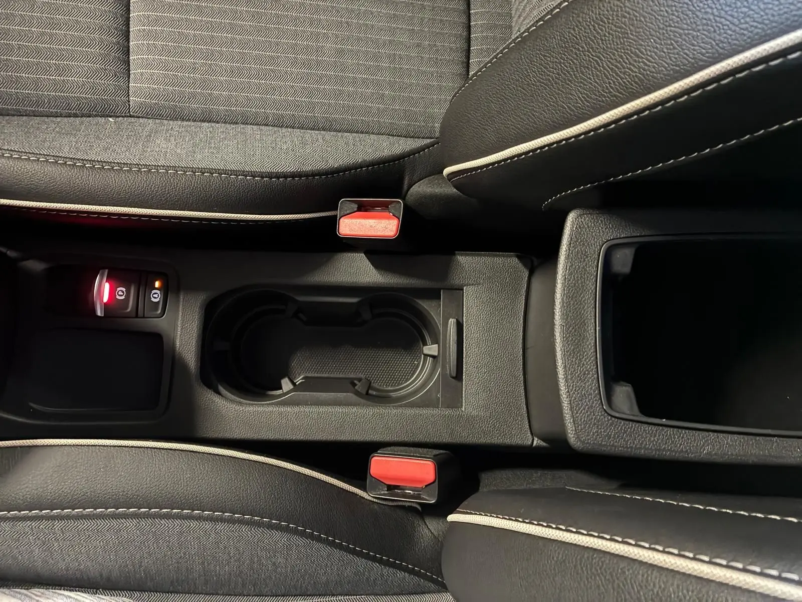 Vue plongeante sur la console centrale de la Renault Clio V E-Tech 145 Techno, avec porte-gobelets et sièges tissu gris noir.