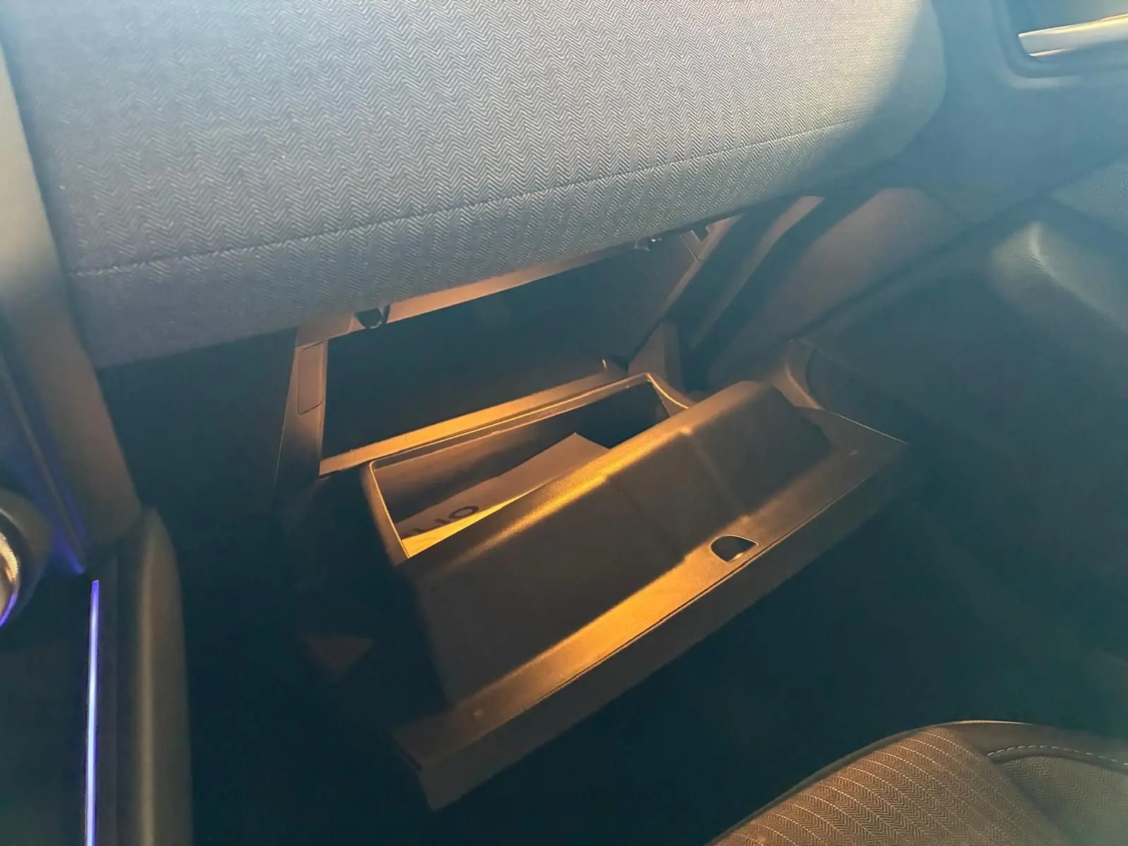 Gros plan de la boîte à gants ouverte côté passager dans l’habitacle gris noir de la Renault Clio V E-TECH 145 TECHNO.