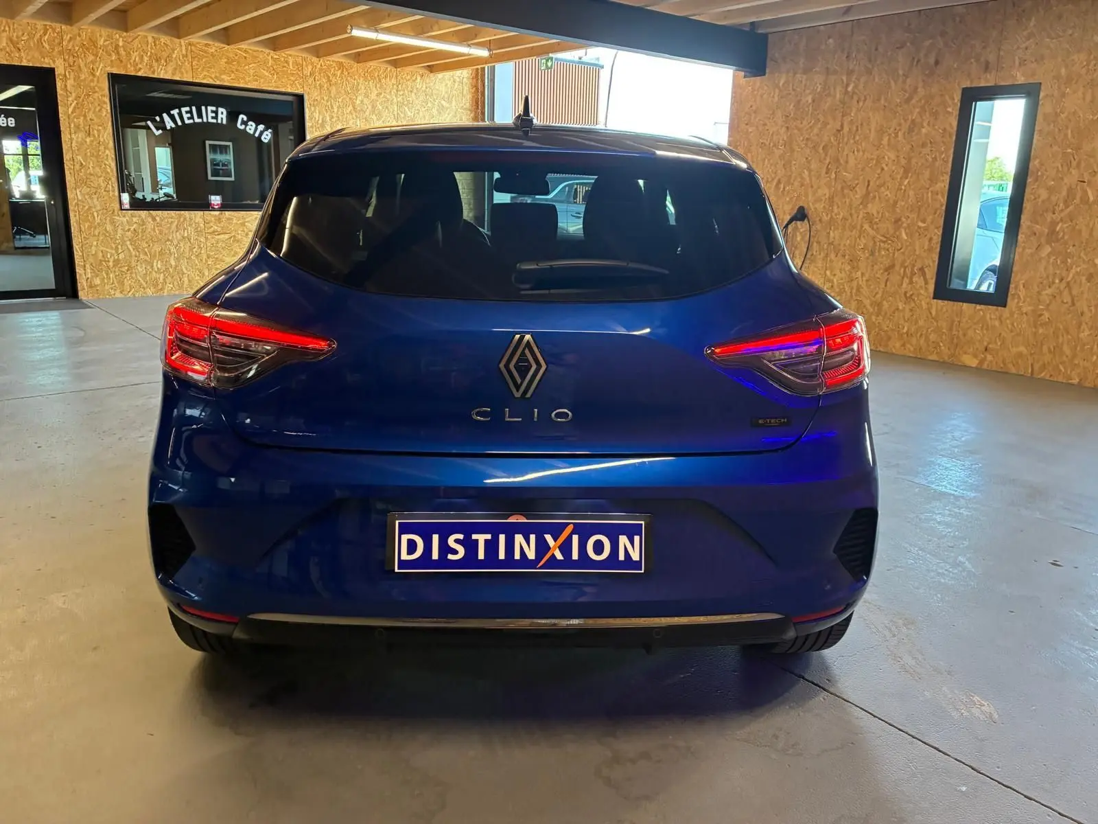 Vue arrière de la Renault Clio V E-Tech 145 Techno bleu Iron, avec feux allumés et plaque Distinxion visible.
