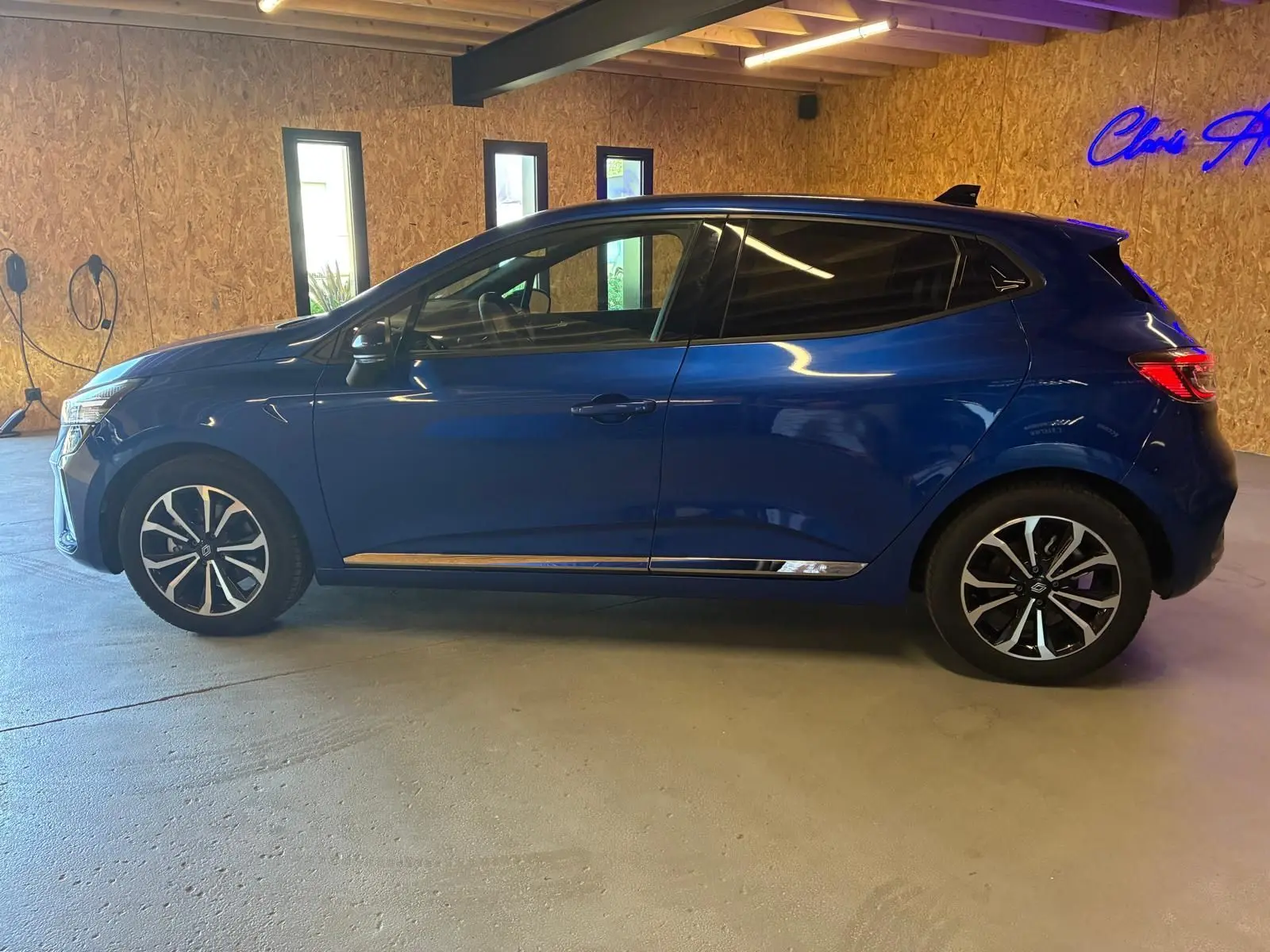 Profil droit d'une Renault Clio V E-TECH 145 TECHNO bleu iron, avec jantes biton et vitres teintées, en intérieur showroom.