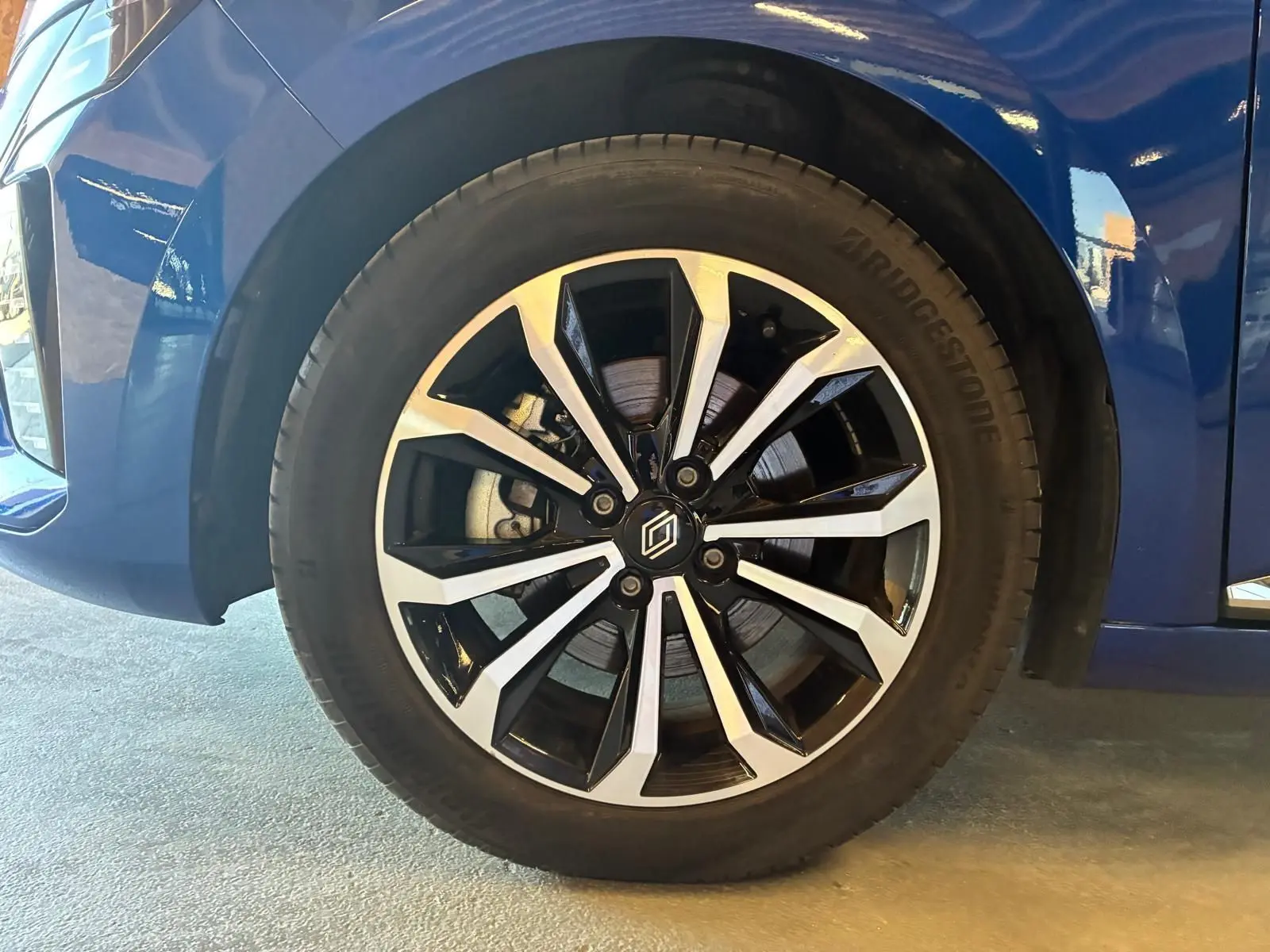 Gros plan sur la roue avant gauche de la Renault Clio V E-TECH 145 TECHNO bleu iron avec jante alliage bicolore.
