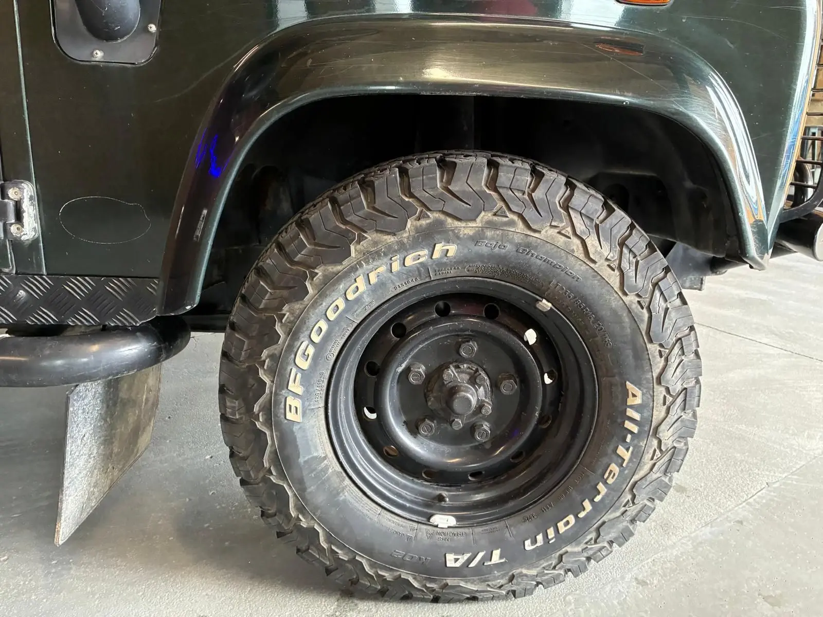 Gros plan sur la roue avant gauche du Land Rover Defender 110 vert 2005 avec pneu BFGoodrich tout-terrain.