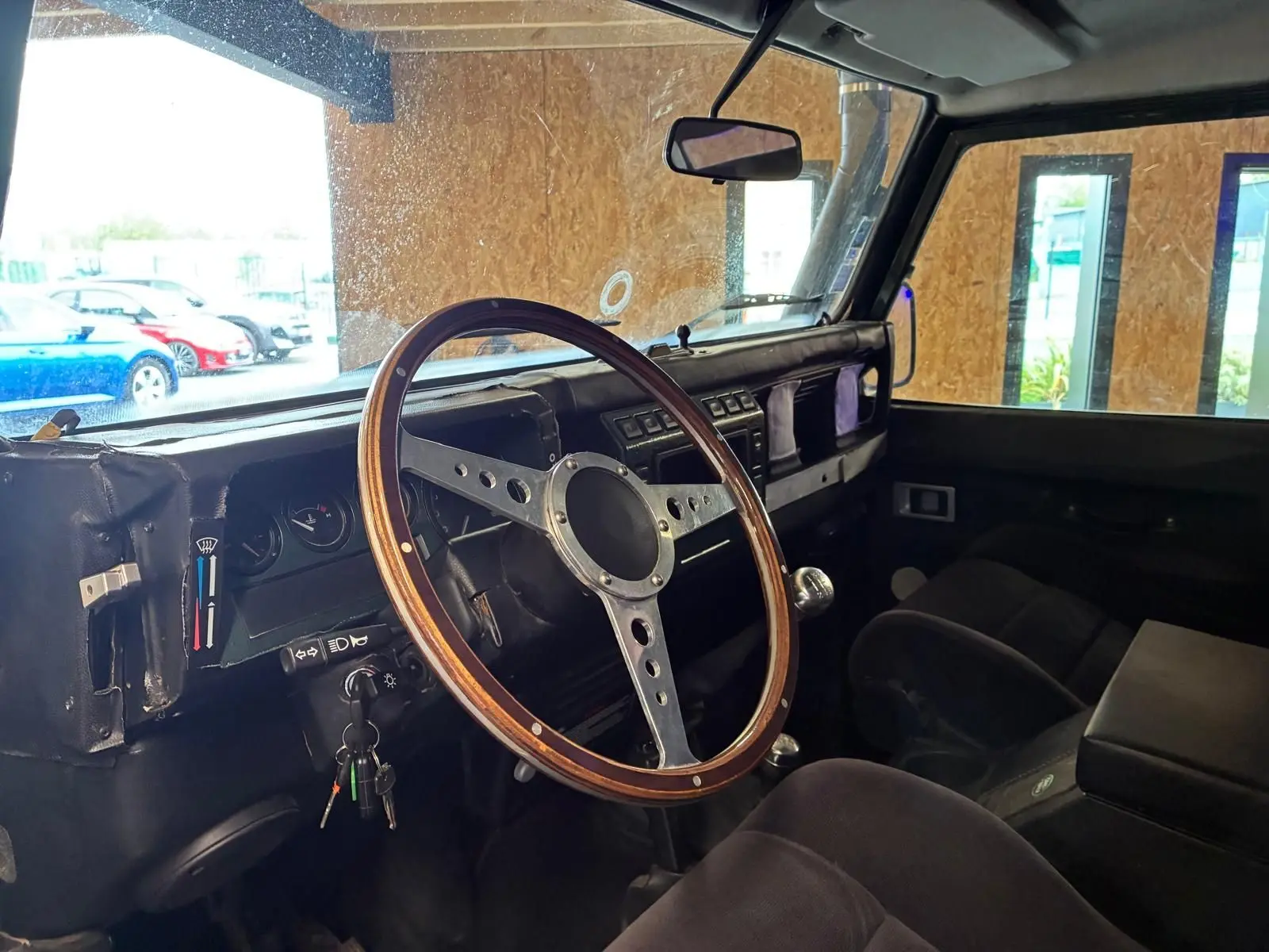 Intérieur du Land Rover Defender 110 vert de 2005, vue côté conducteur, volant bois vintage et tableau de bord simple.
