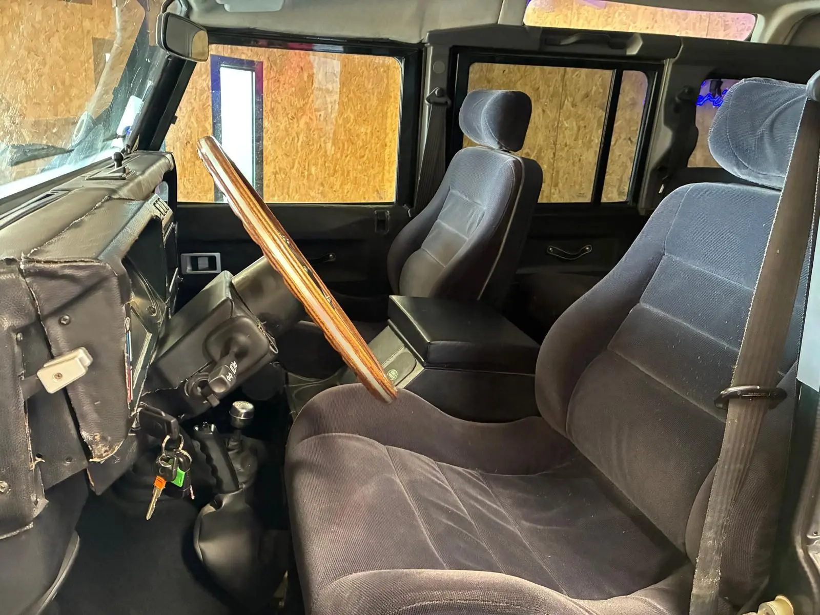 Vue intérieure côté conducteur du Land Rover Defender 110 2005, avec volant bois et sièges noirs en tissu.